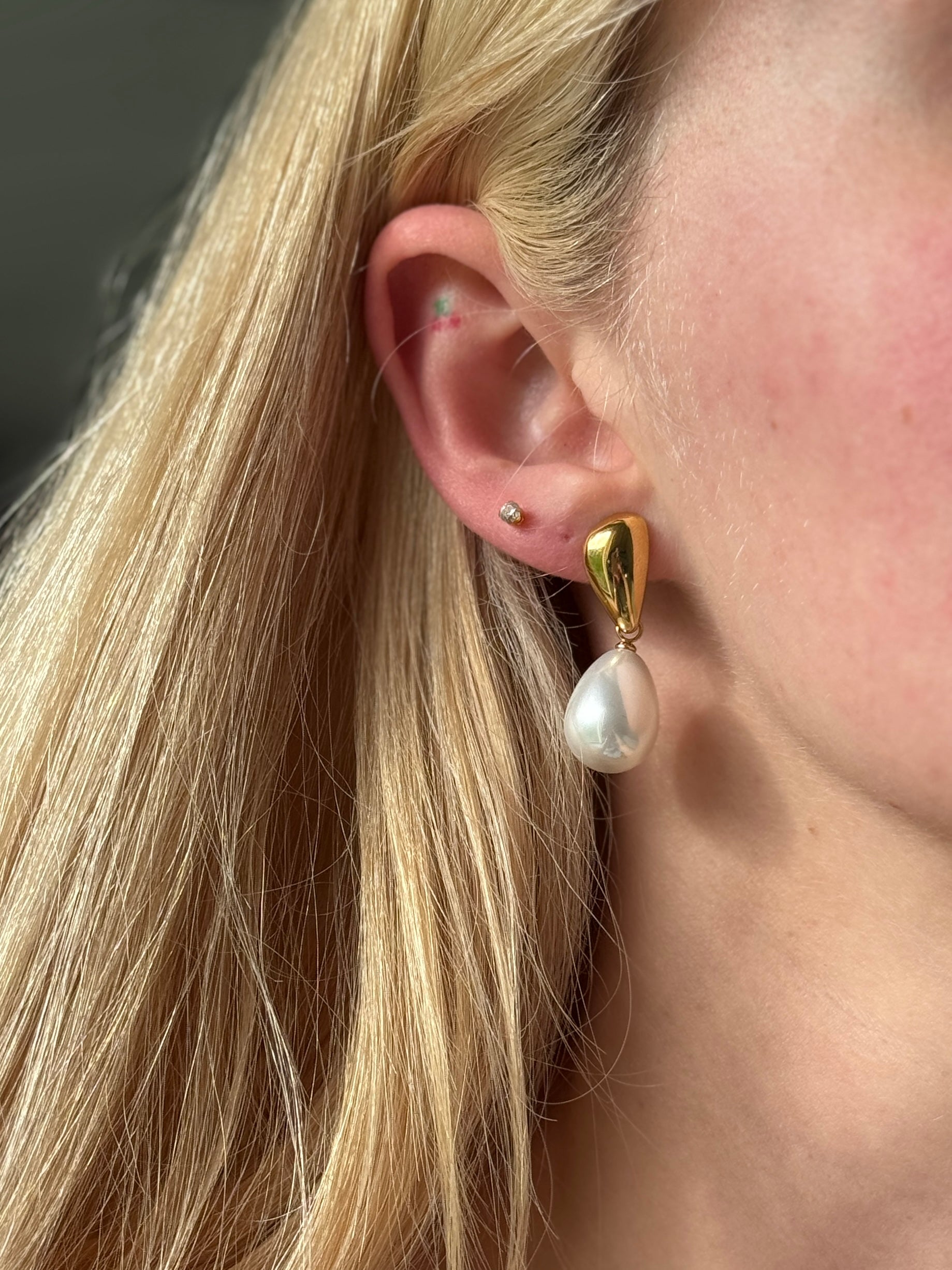 Close-up of a person wearing a stainless steel pearl earring with a gold setting.