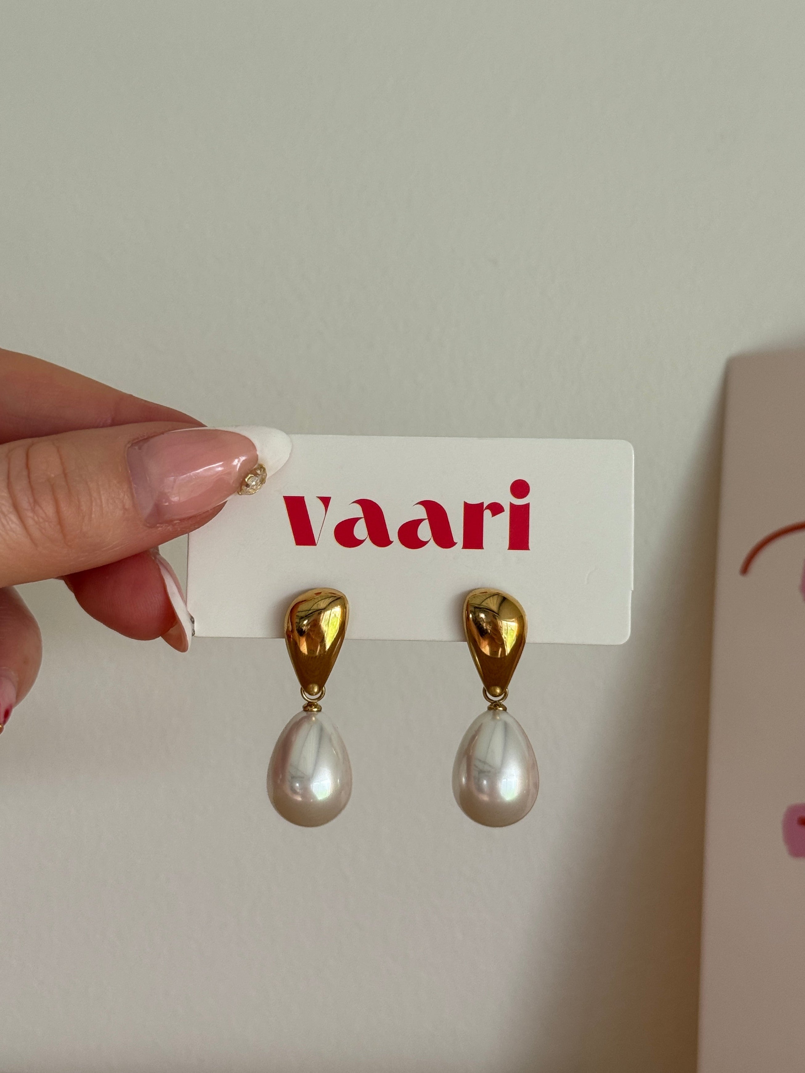 Gold and pearl drop earrings on a 'Vaari' branded card held by a hand. Stainless steel & waterproof jewelry.