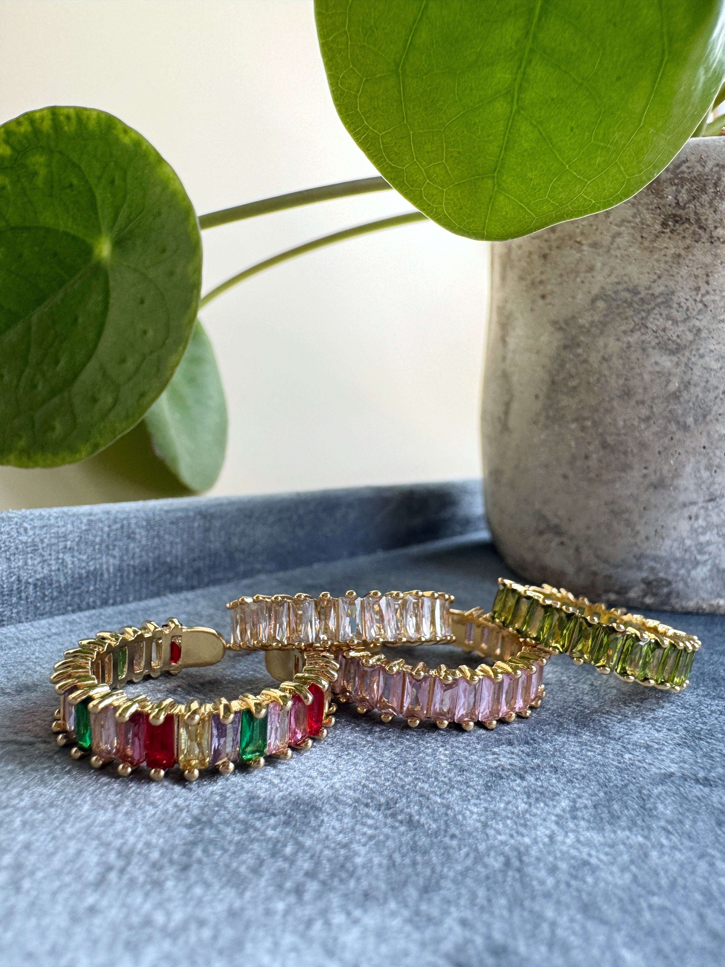 Three in size adjustable golden rings with colorful gemstones on a blue surface with green leaves in the background