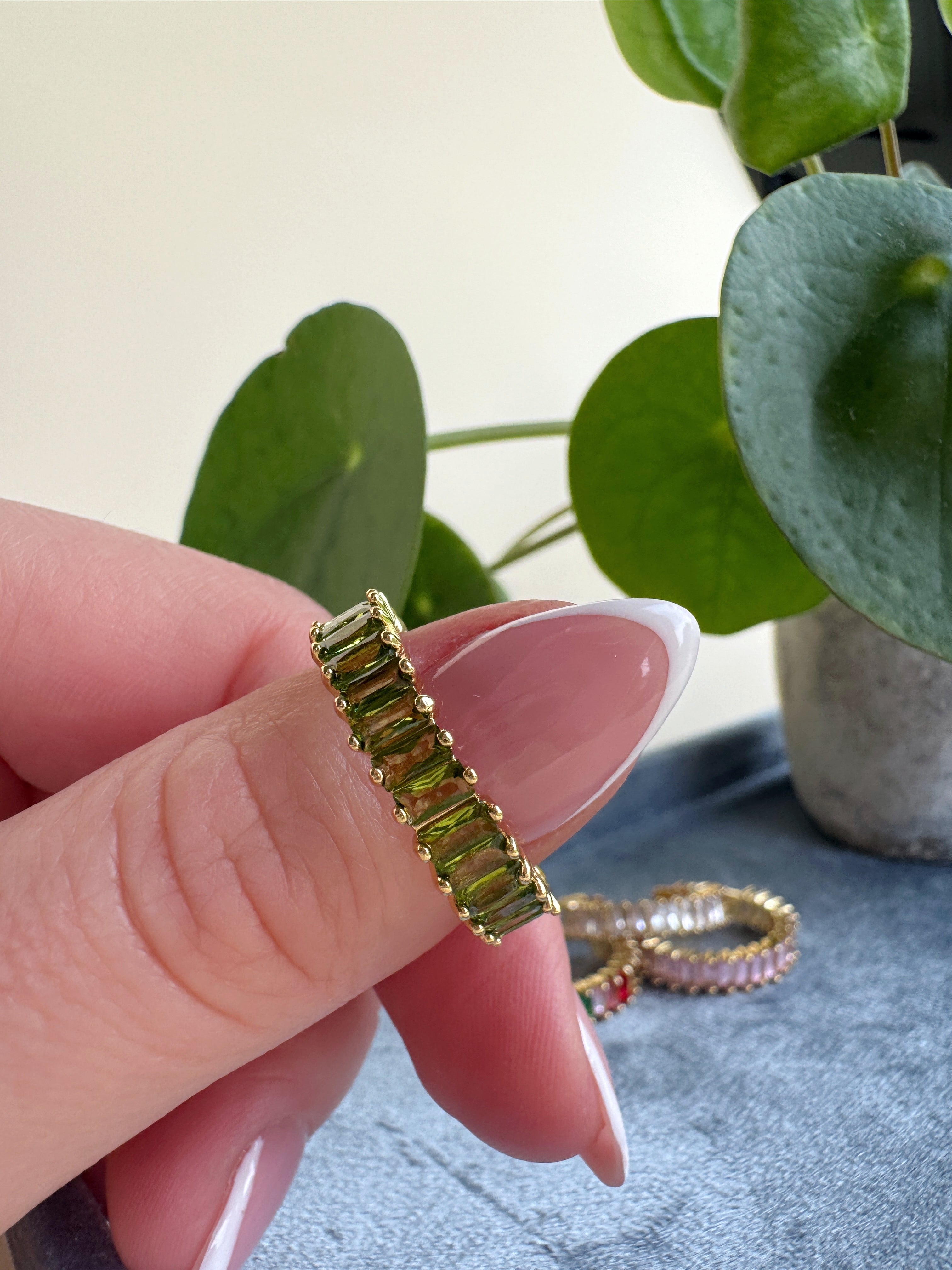 French manicured thumb holding an adjustable green beaded ring with a plant in the background