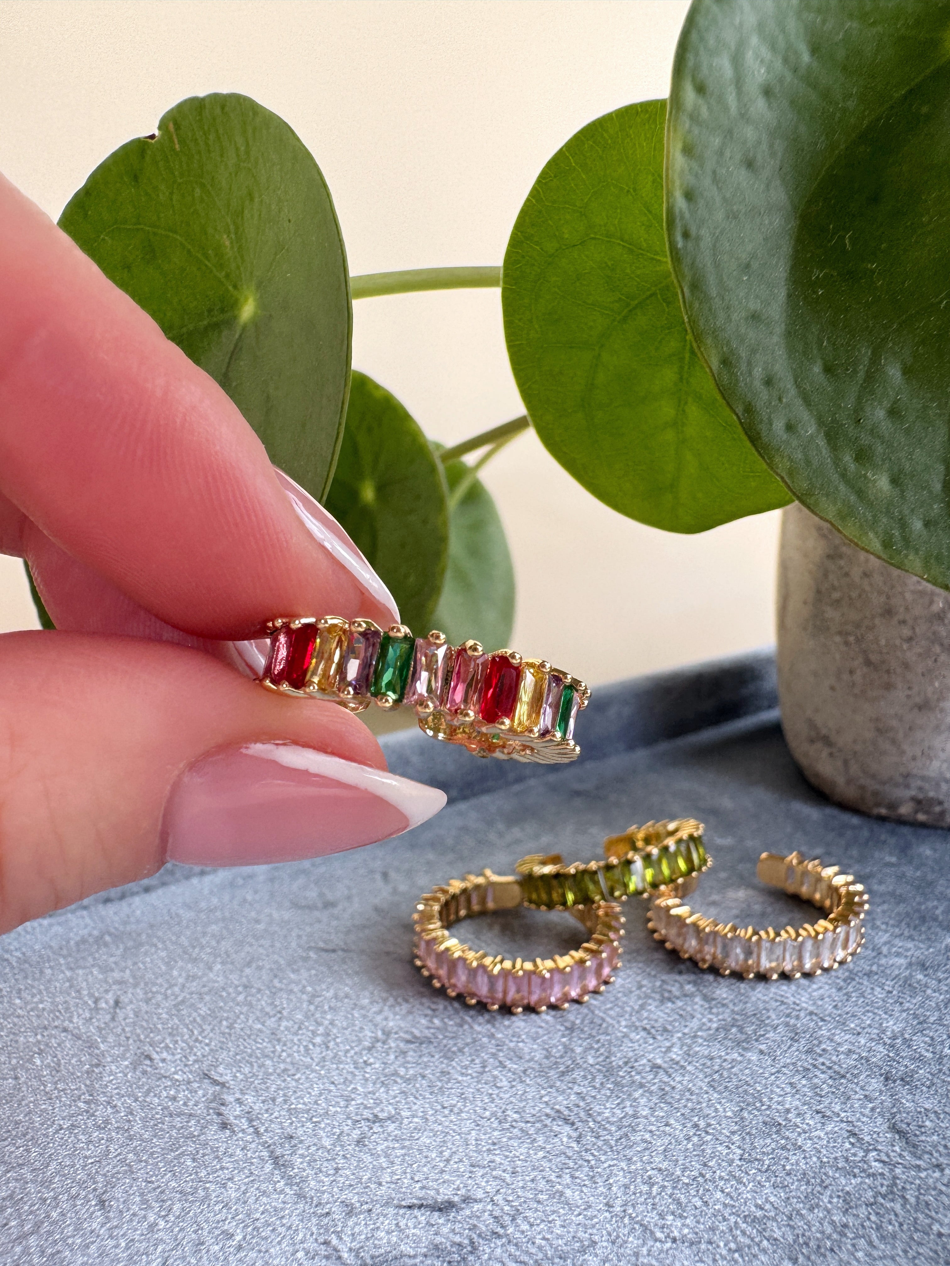 Adjusatble size multicolor ring held by a french manicured hand with a plant in the background