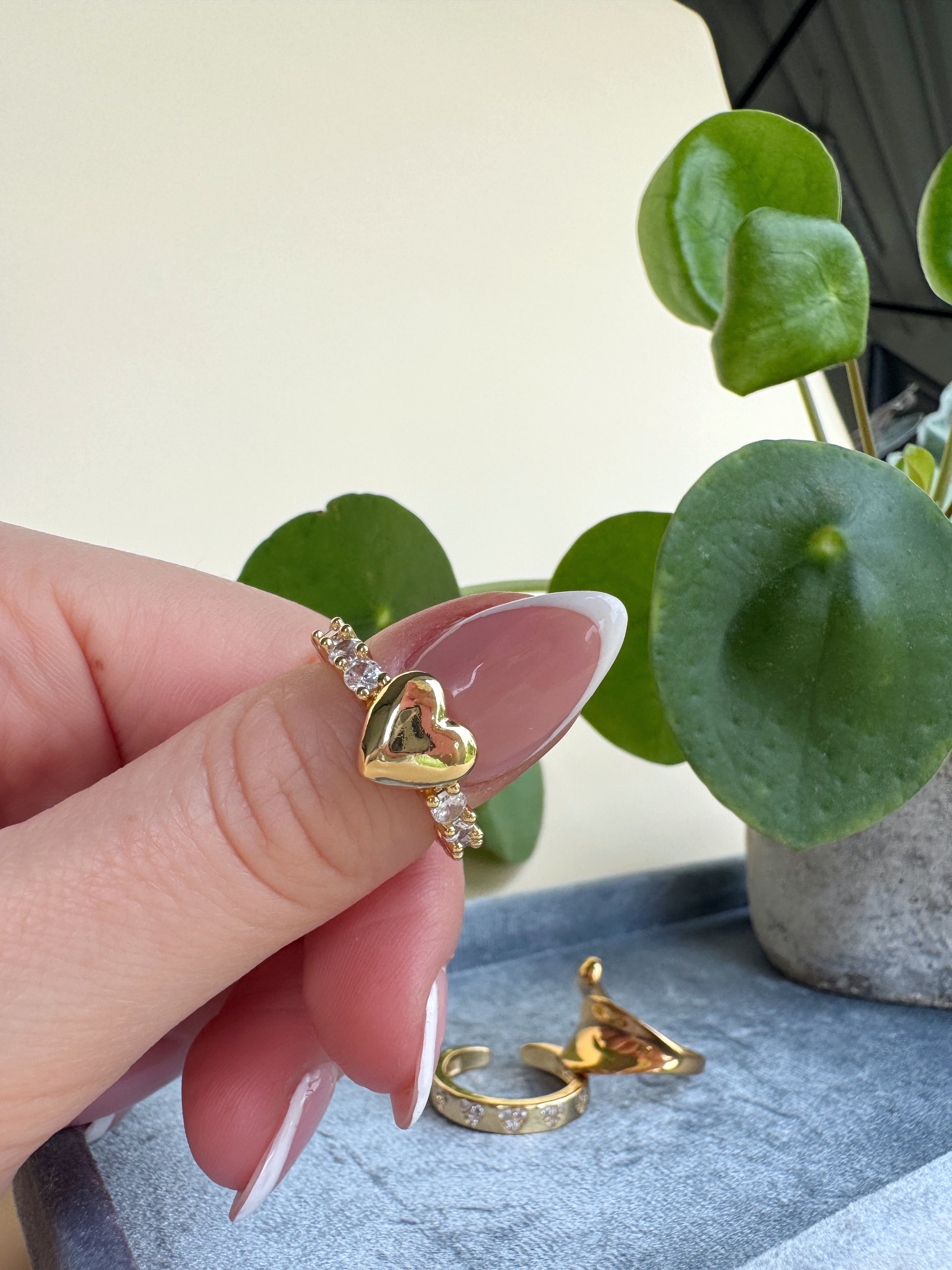 Heart-shaped gold ring with diamonds on a hand against a light background
