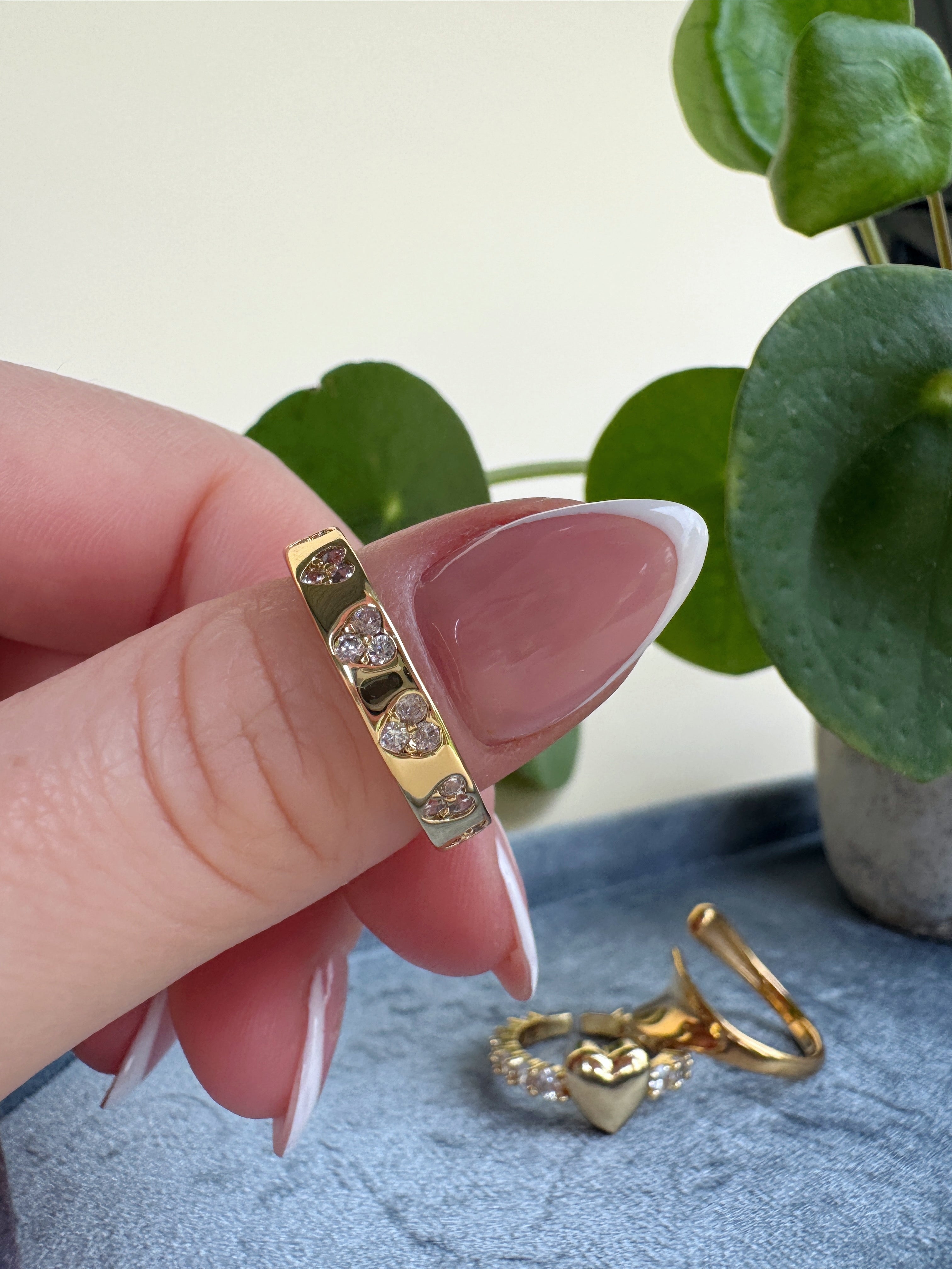 Gold ring with heart-shaped stones held by a hand against a light background