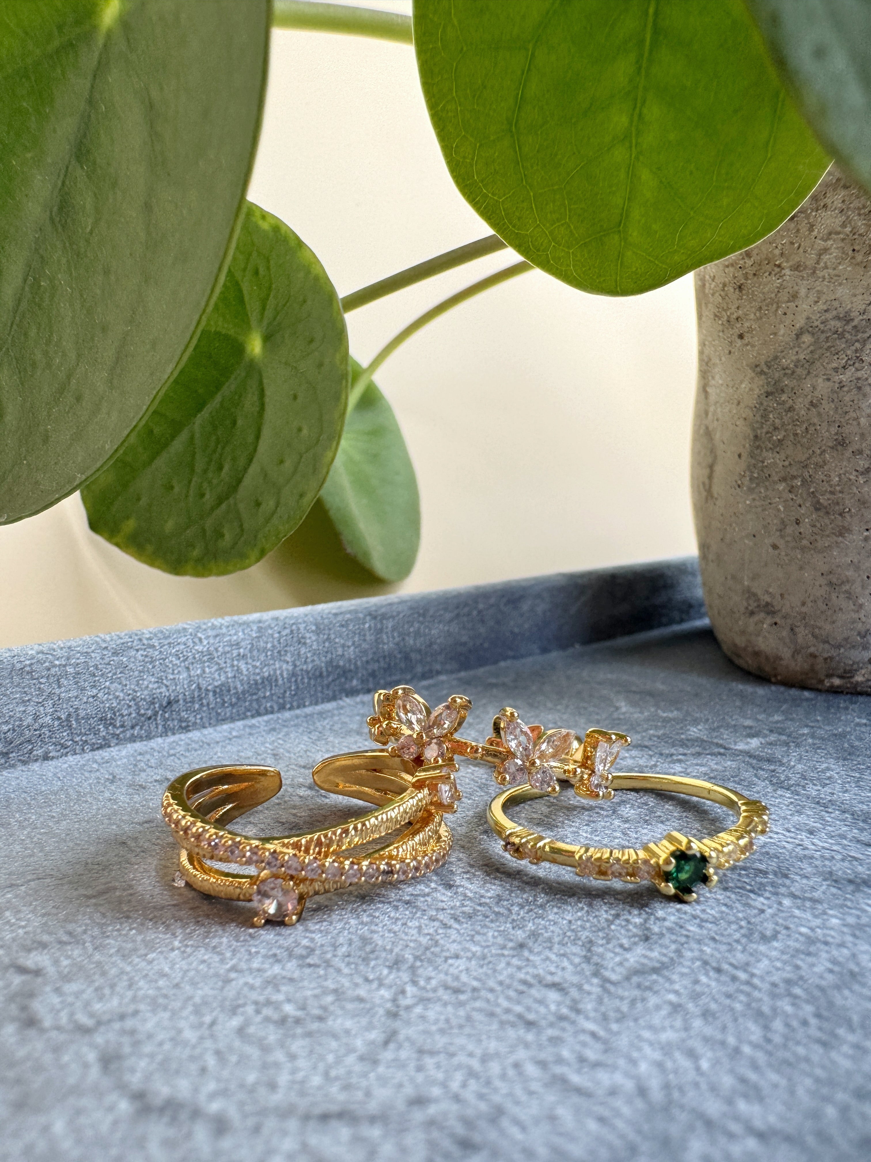 Beautiful set of gold rings with gemstones on a textured surface with green leaves in the background