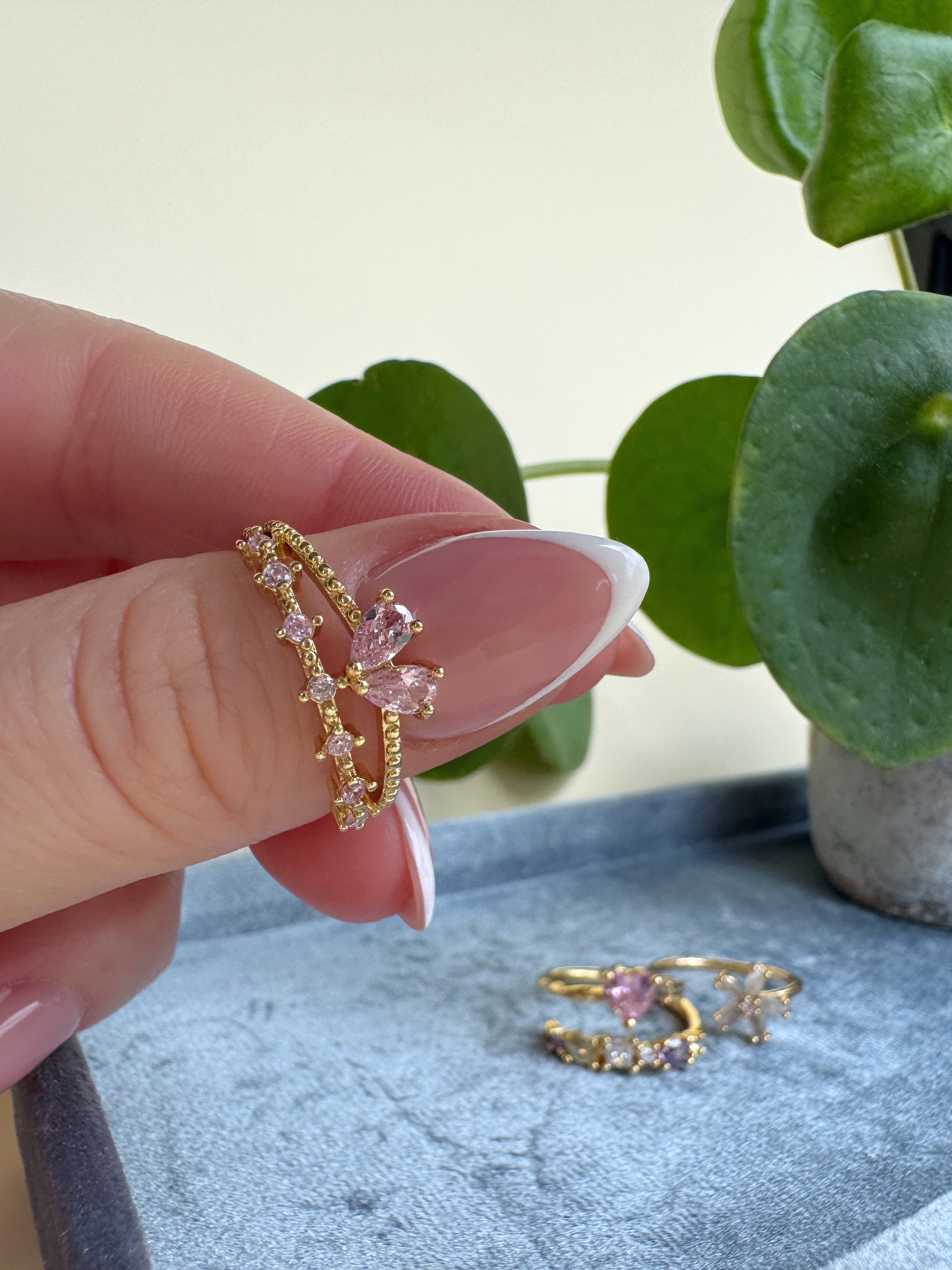 Girly gold ring with pink gemstones held by a hand against a light background