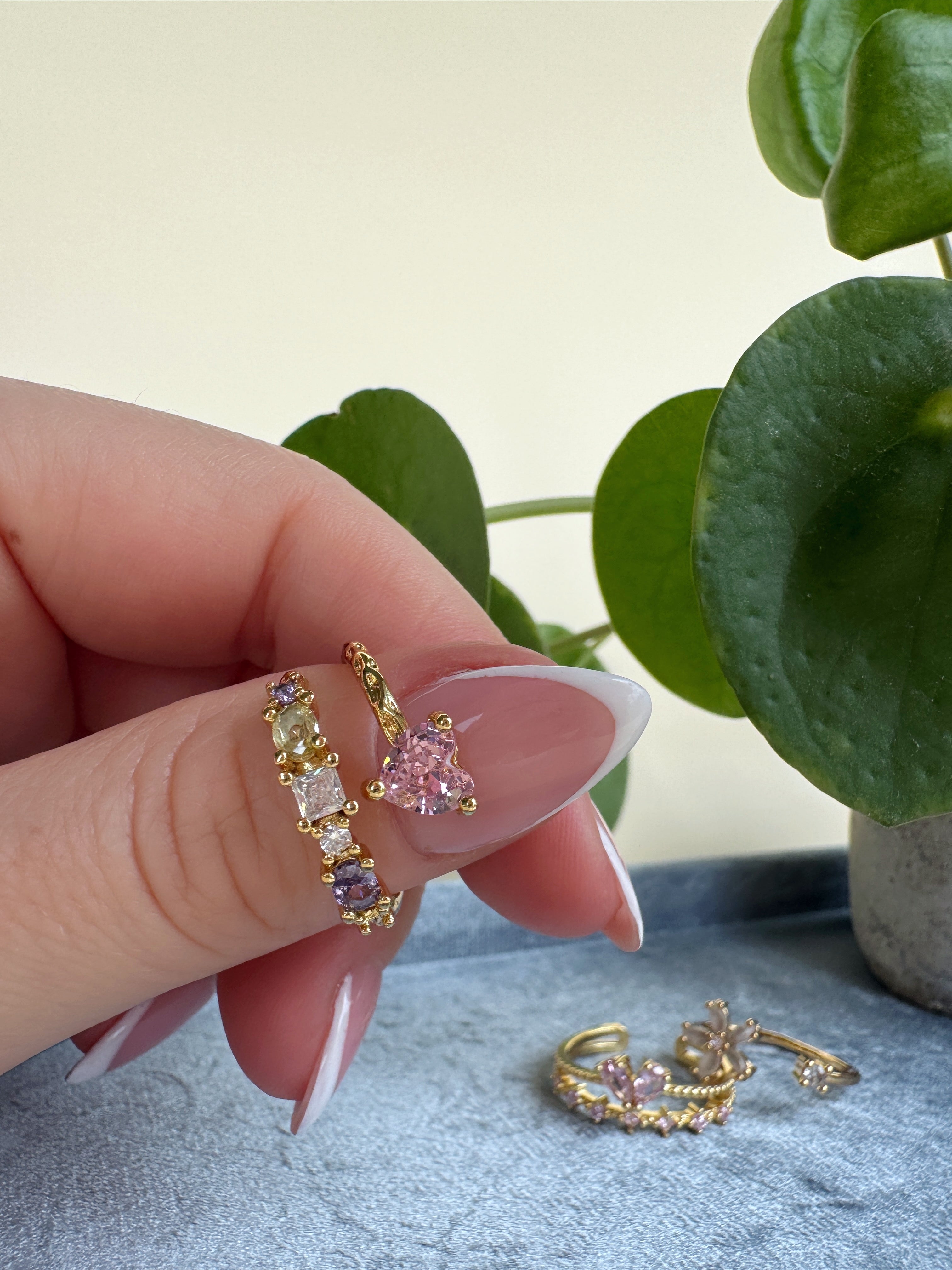 Hand holding gold and pink feminine ring with a plant in the background