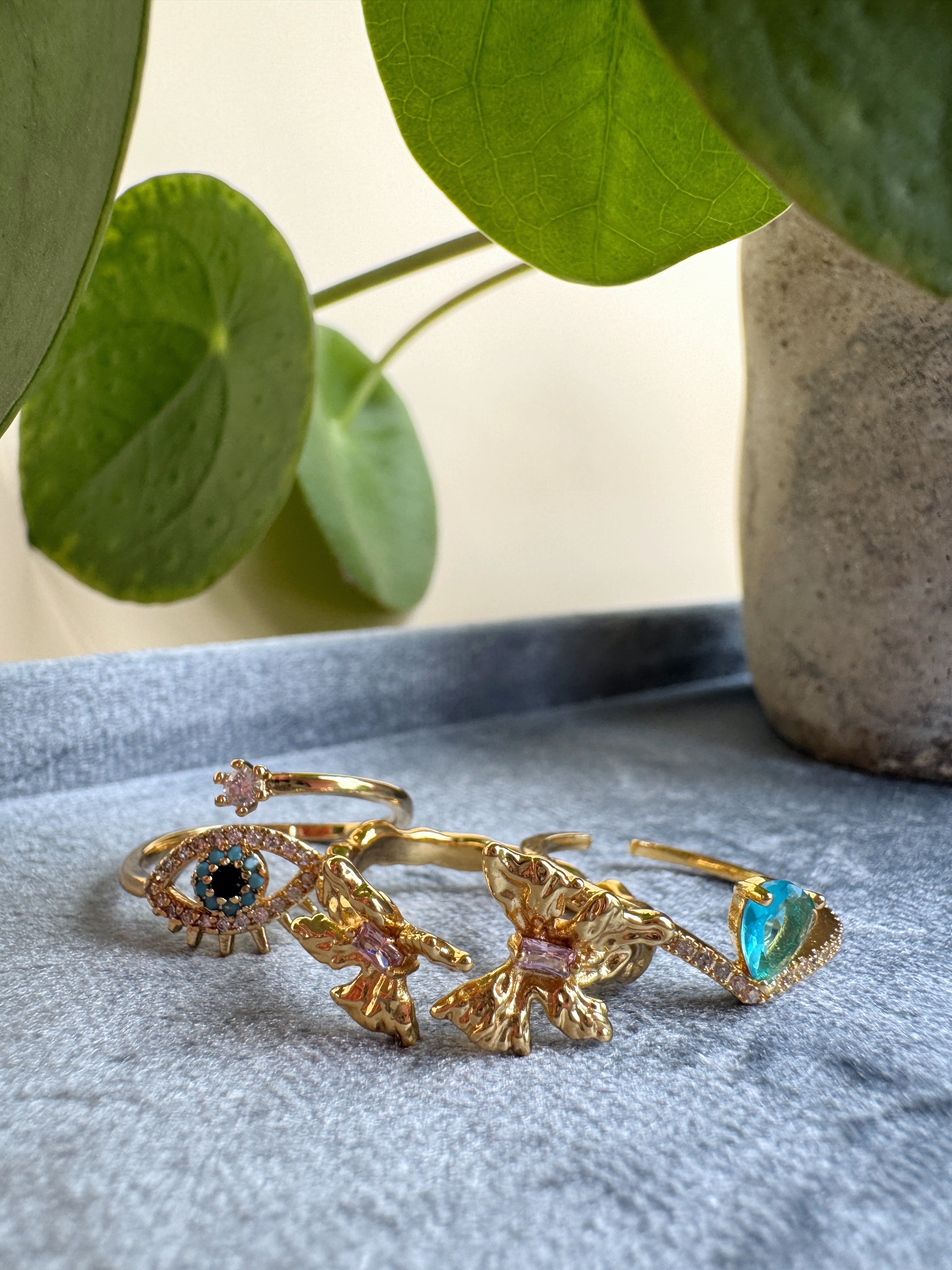 Gold rings with gemstones on a textured surface with a plant in the background