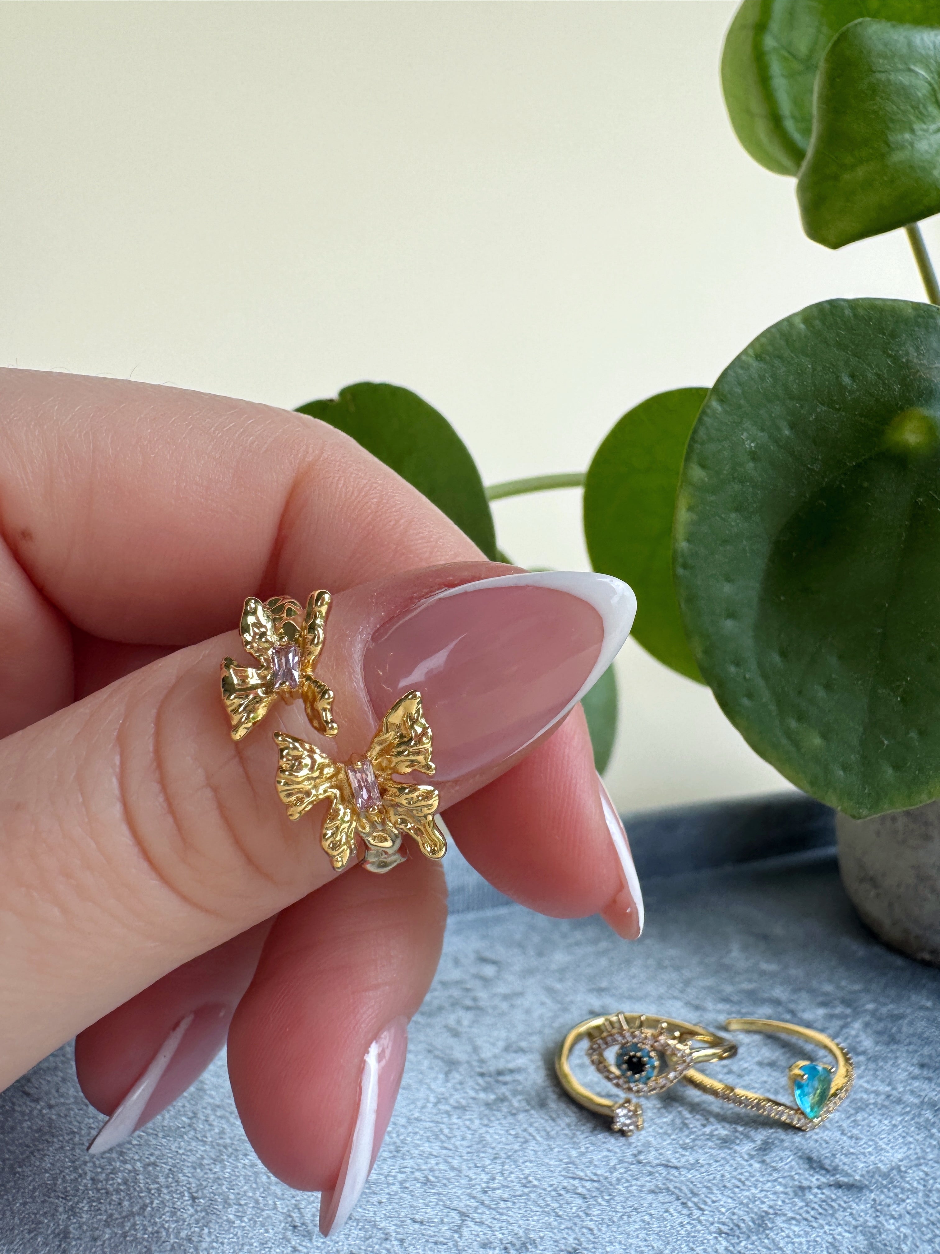 Gold unique organic shaped ring held by a french manicured hand with a light background