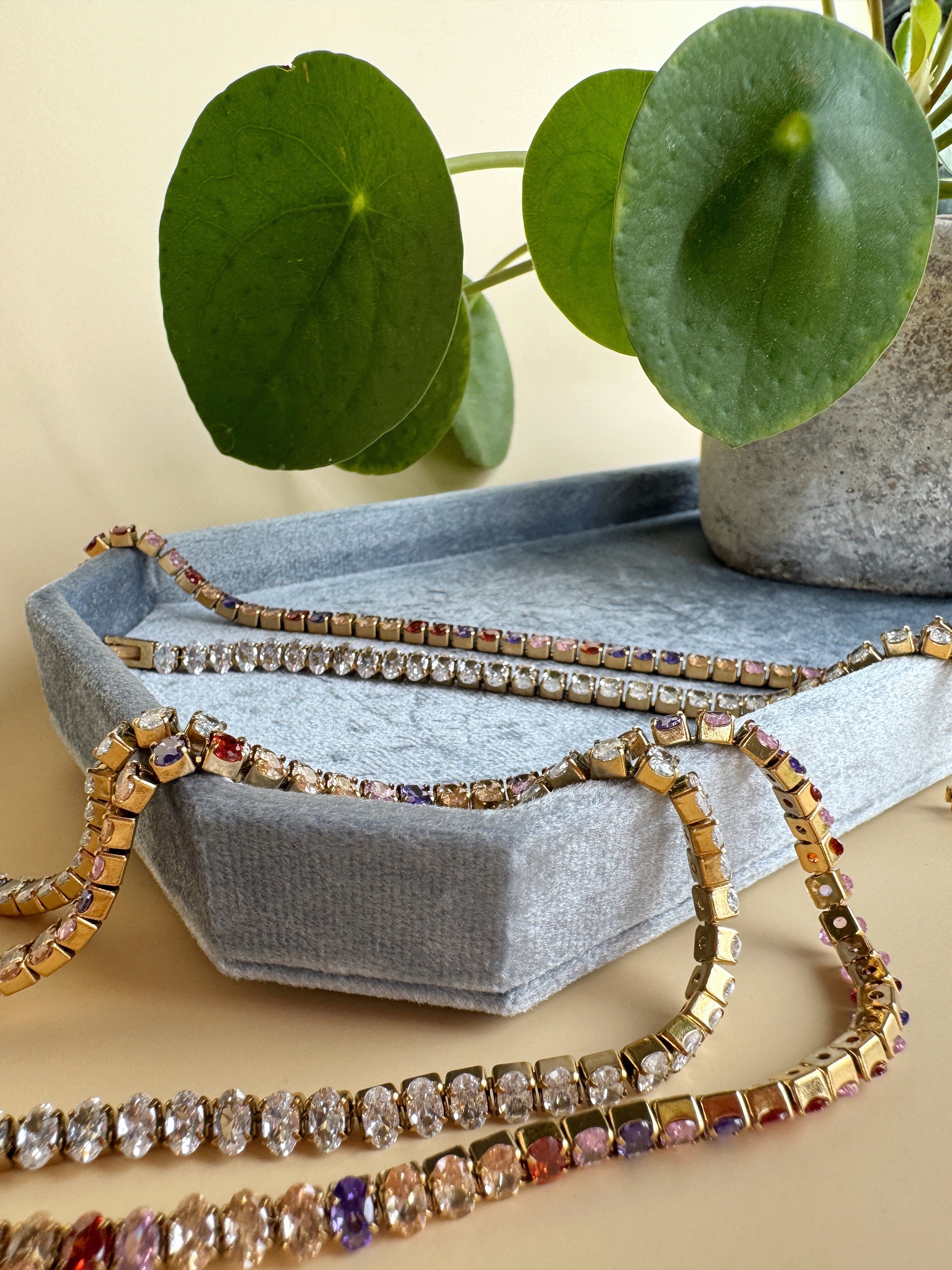 Colorful beaded bracelets on a textured surface with a plant in the background