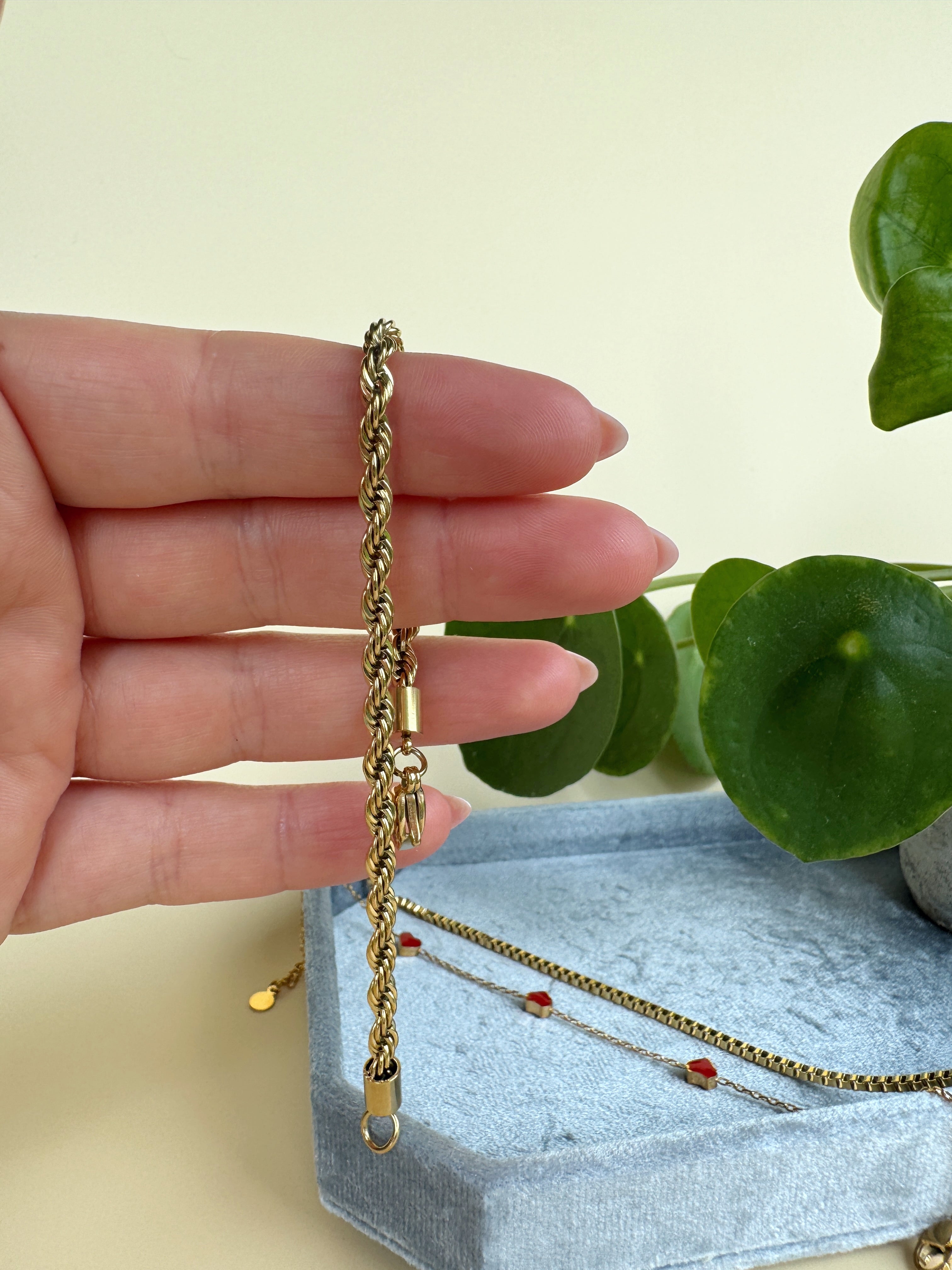 Gold bracelet held by a hand with a light background
