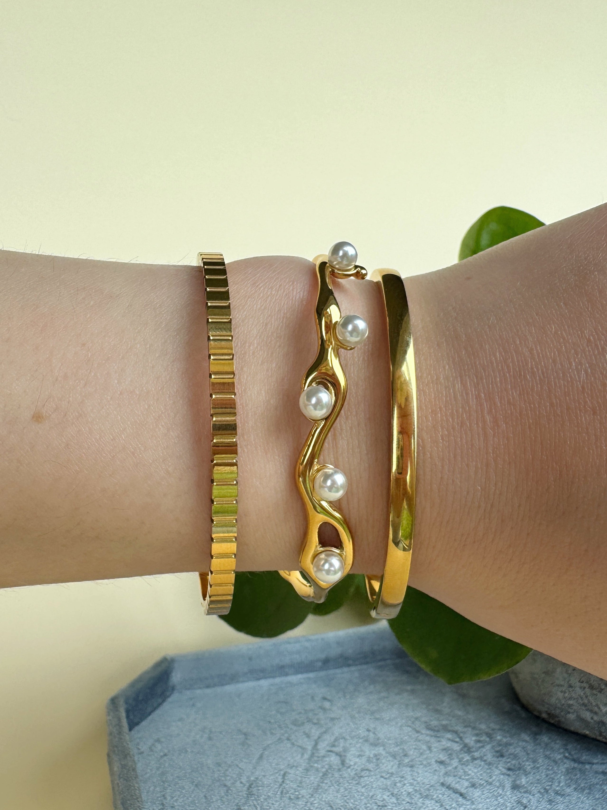 Gold bracelets with pearl accents on a wrist against a neutral background