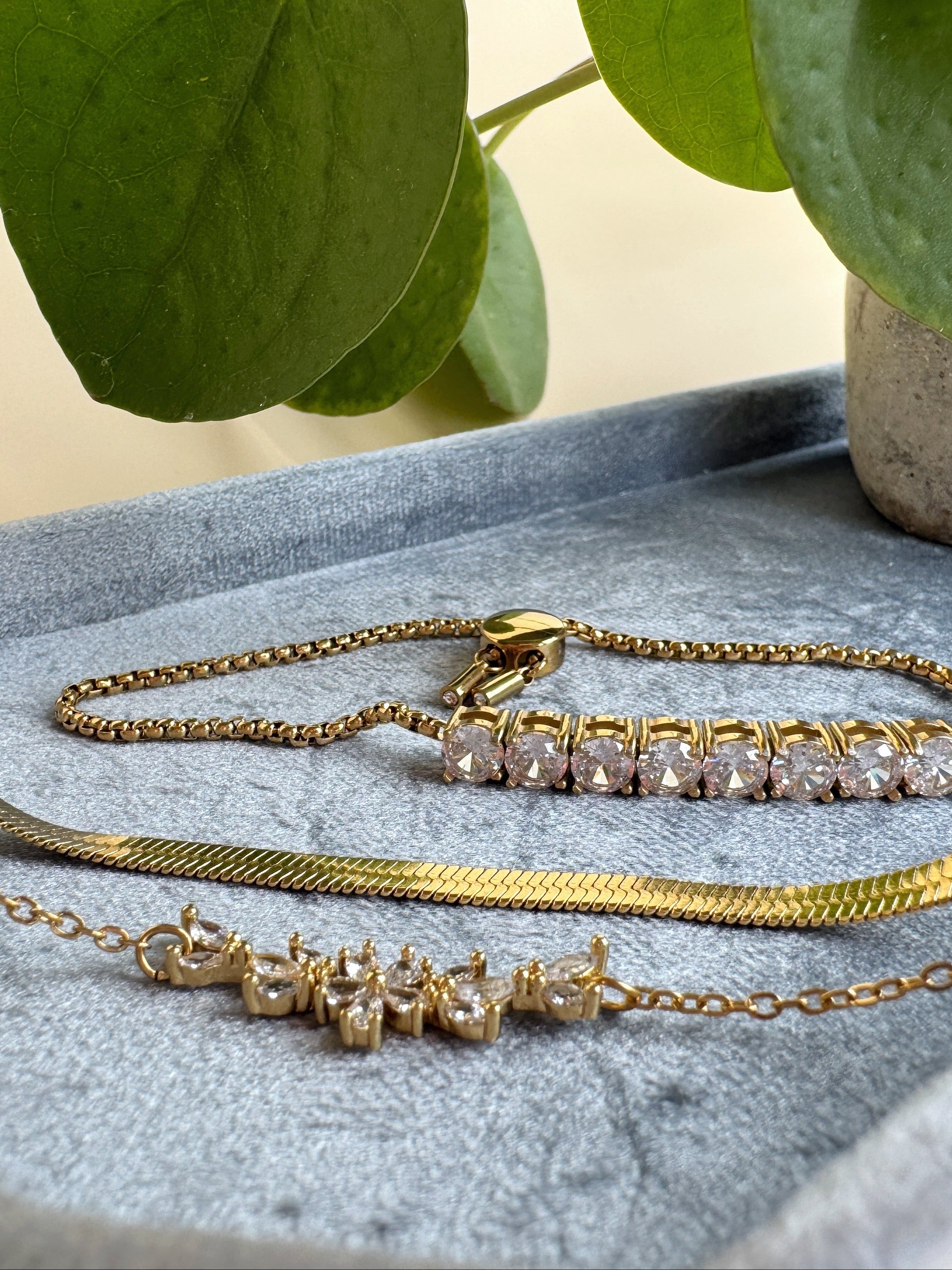Gold necklaces with gemstones on a textured surface with green leaves in the background