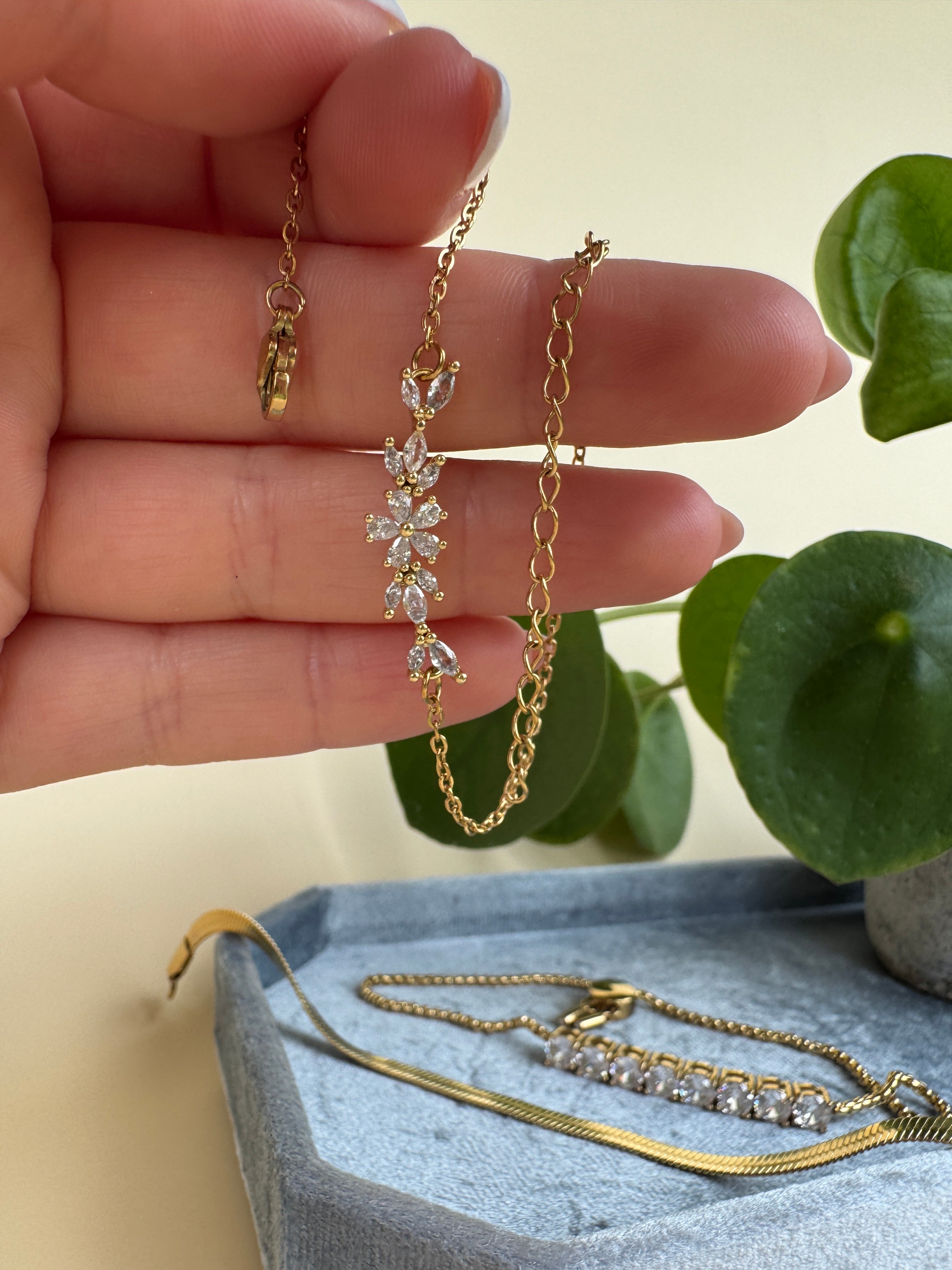 Hand wearing multiple gold necklaces with a light background