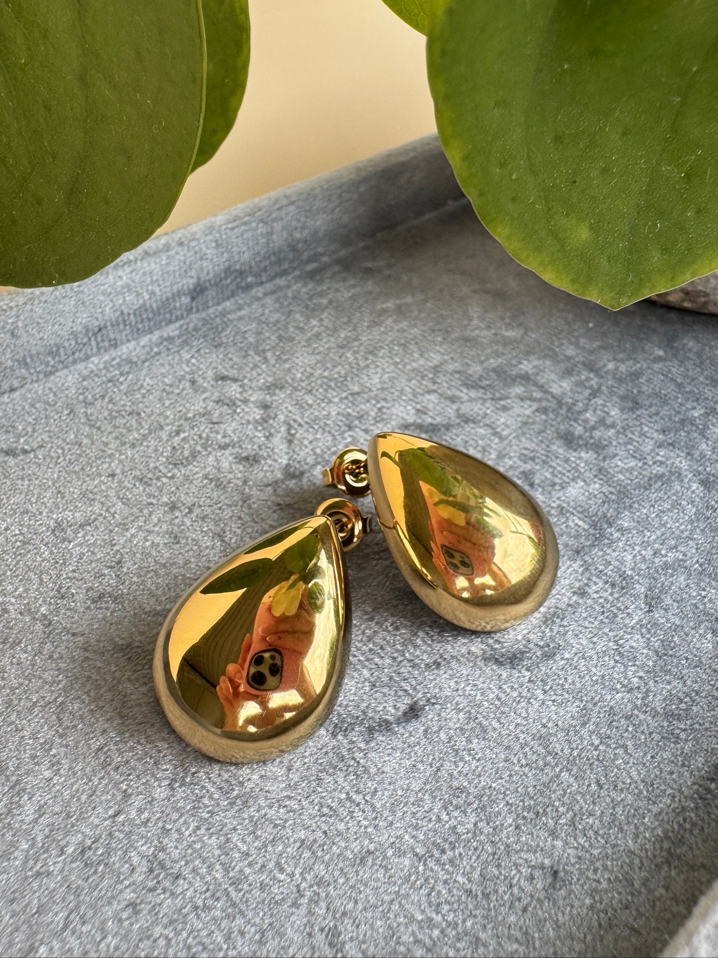 Gold waterproof teardrop earrings on a textured surface with green leaves in the background