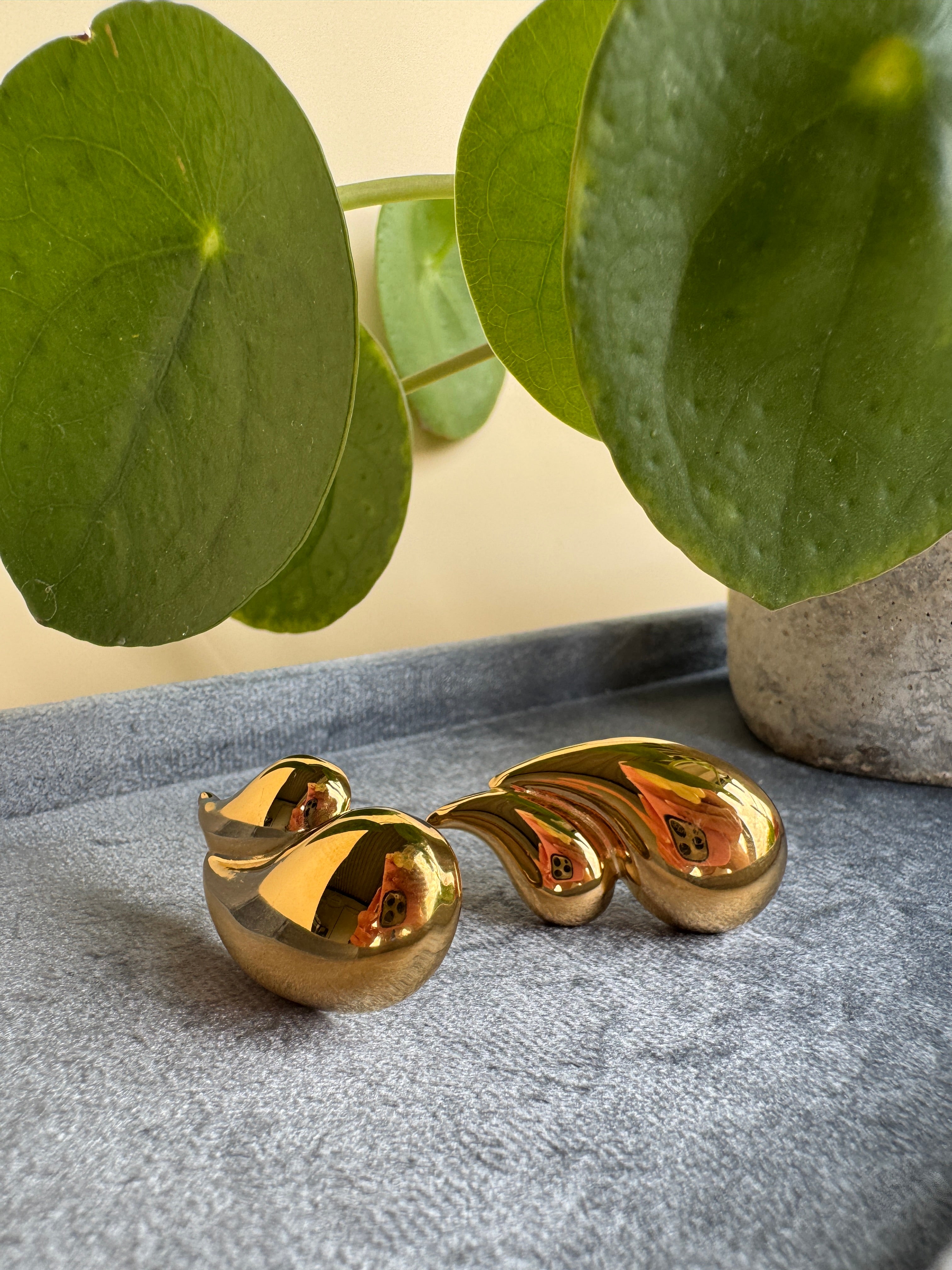 Elegant gold leaf-shaped earring on a gray surface with green leaves in the background