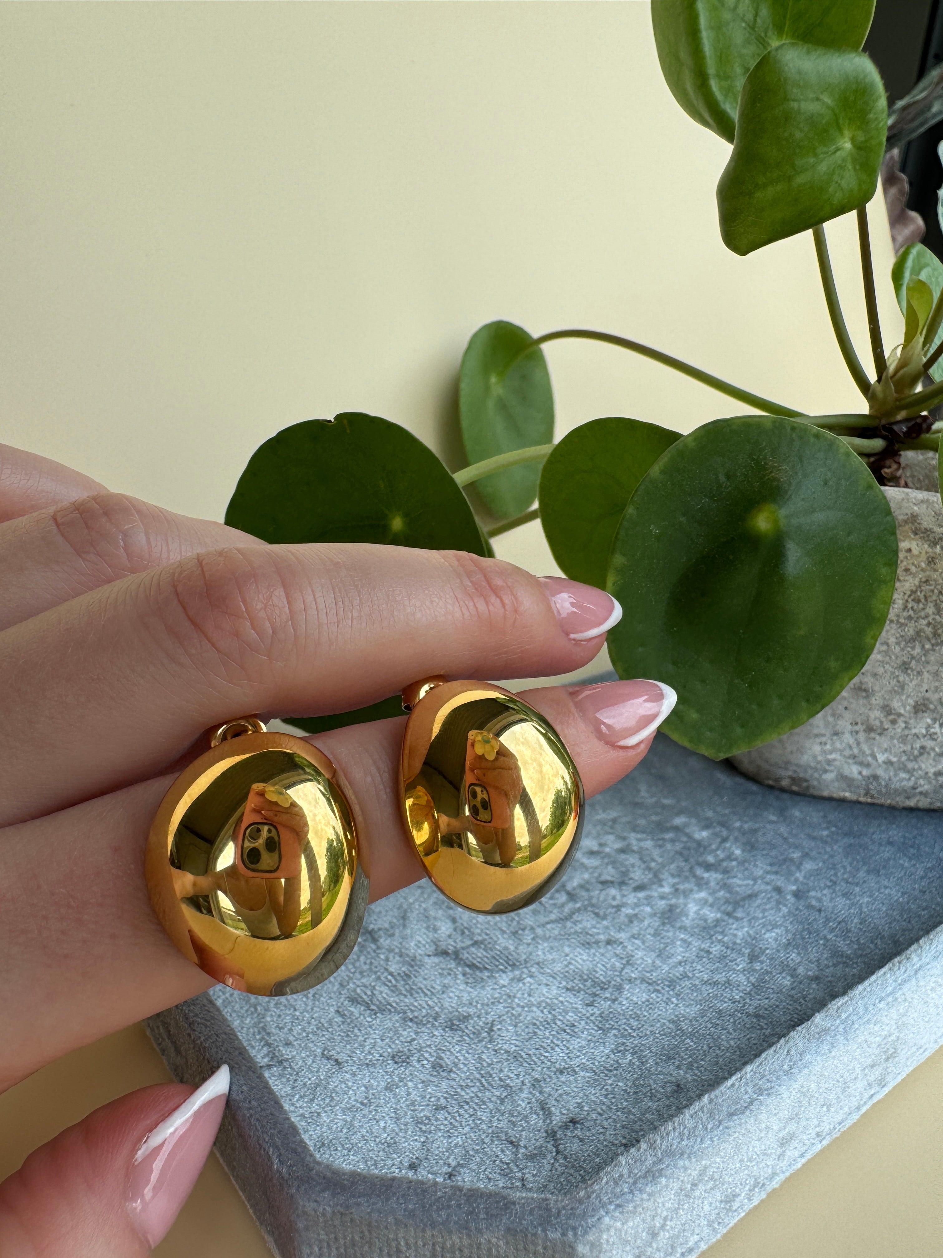 Gold stainless steel earrings being held by a hand with a neutral background