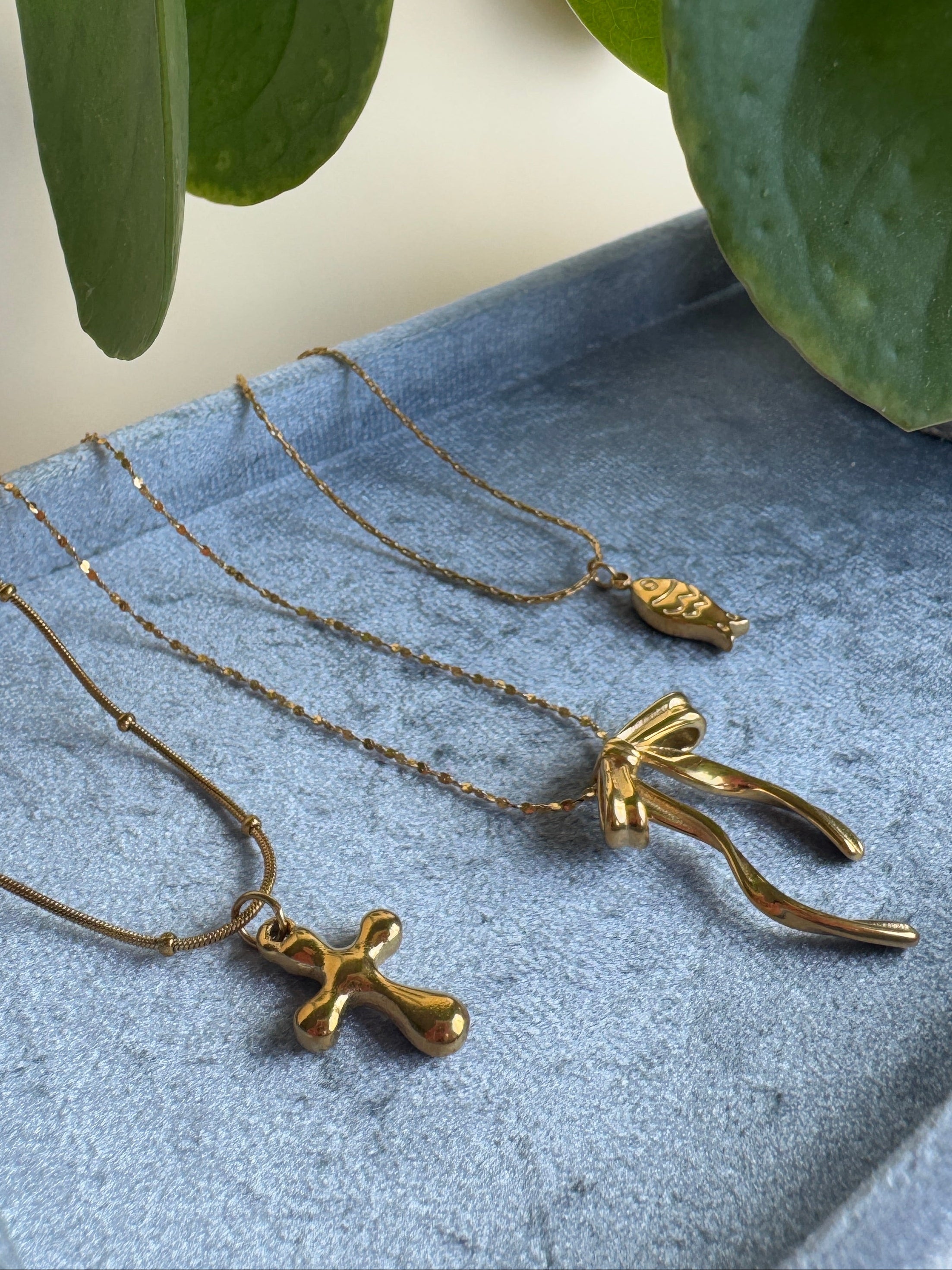 Gold stainless steel necklaces displayed on a textured surface with green leaves in the background