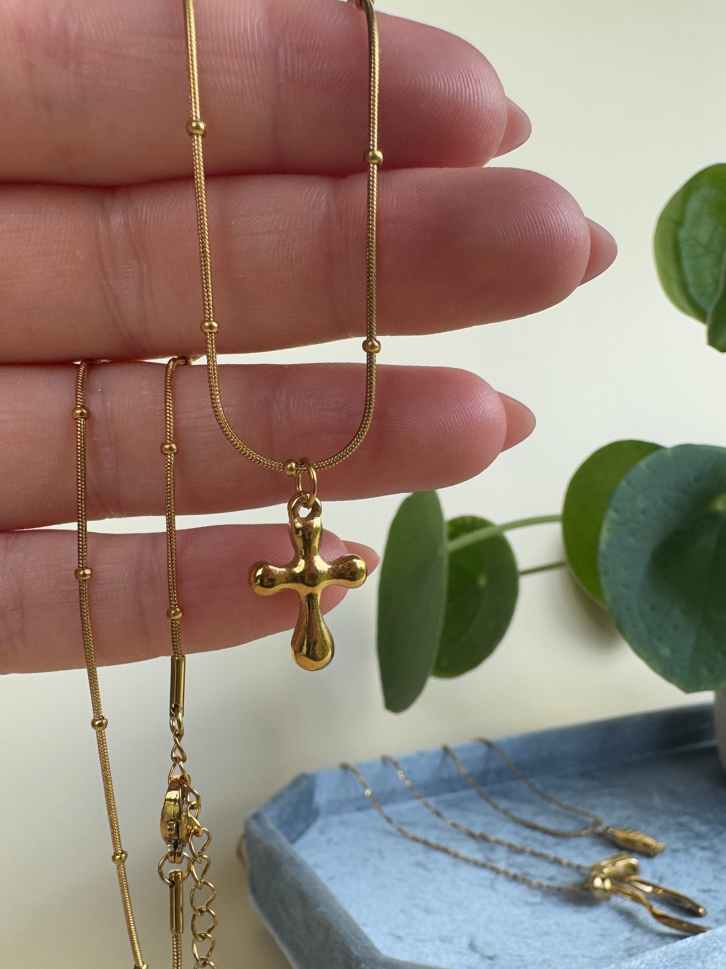 Chubby gold cross necklace being worn on a finger with a light background