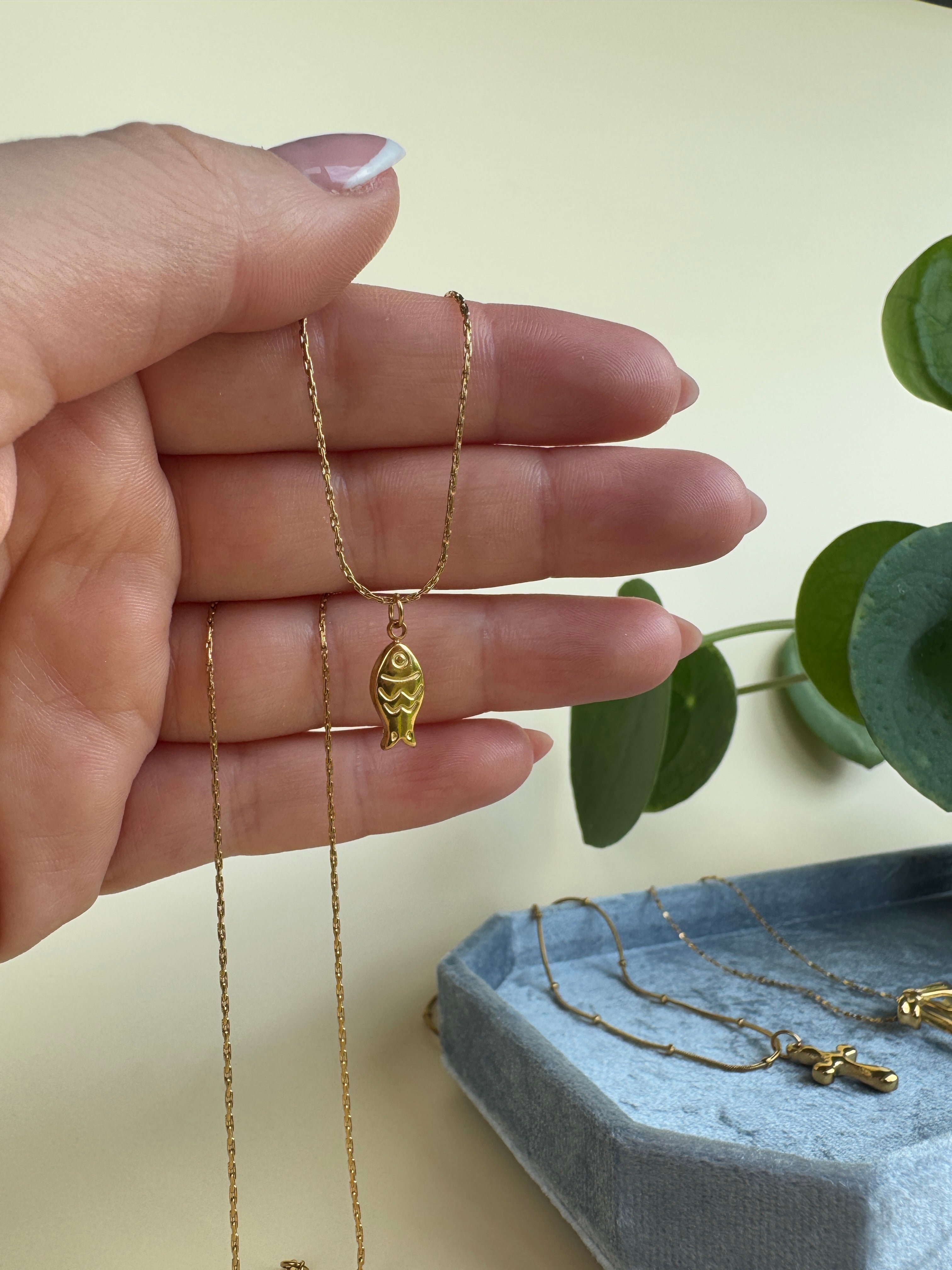 Hand hold a golden fish necklace in front of a light background