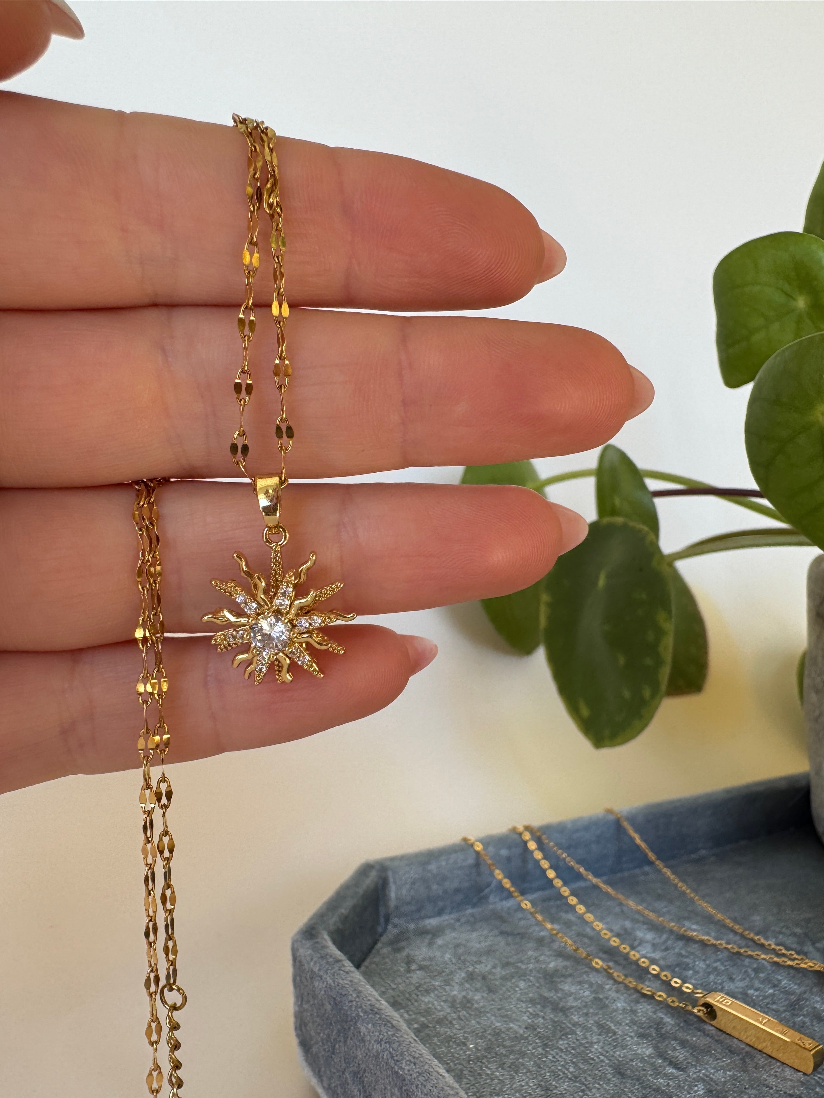 Gold waterproof jewelry on a hand with a plant in the background.