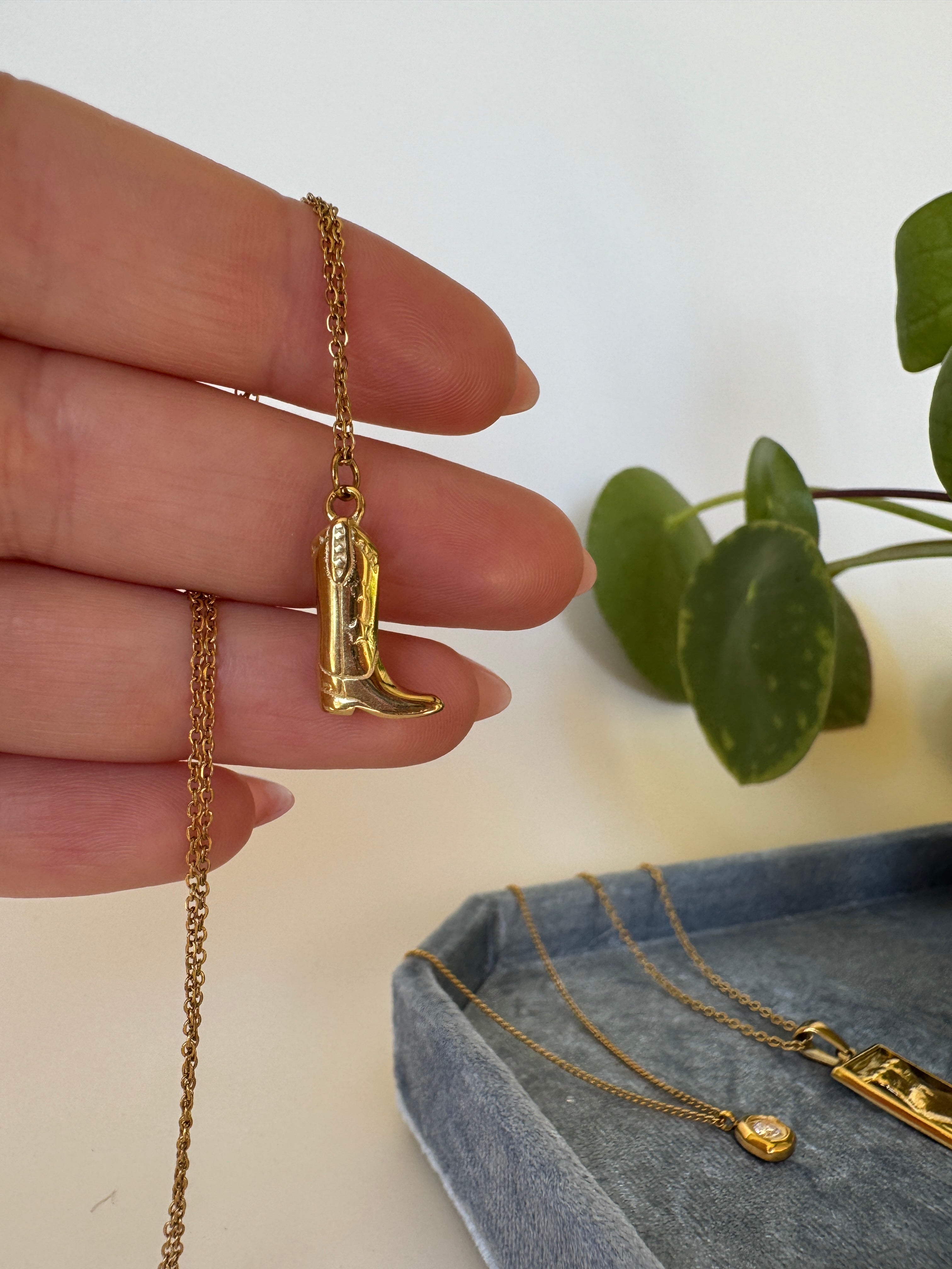 Gold waterproof cowgirl necklace on a hand with a plant in the background