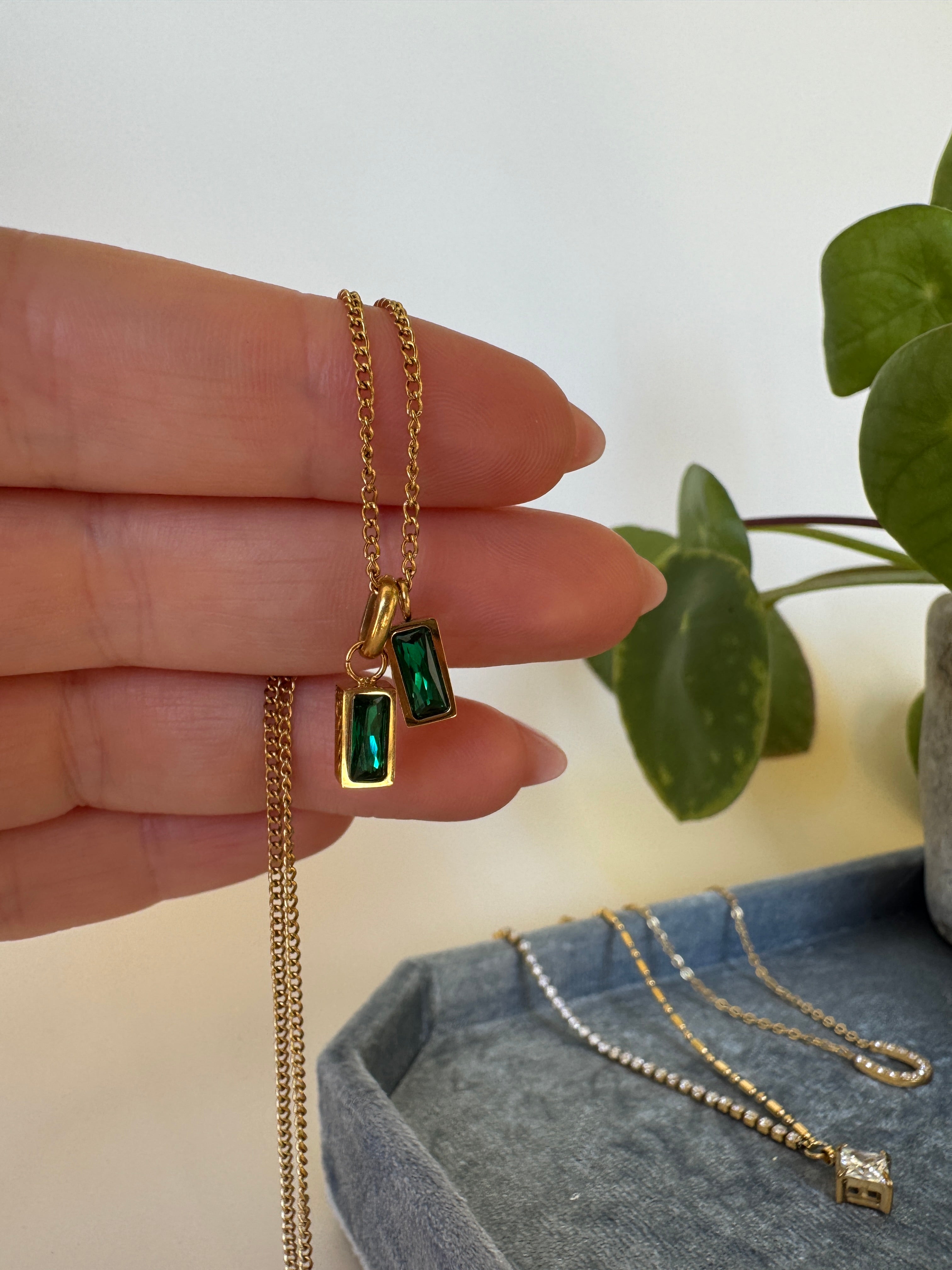 Gold necklace with green gemstones held by a hand against a neutral background