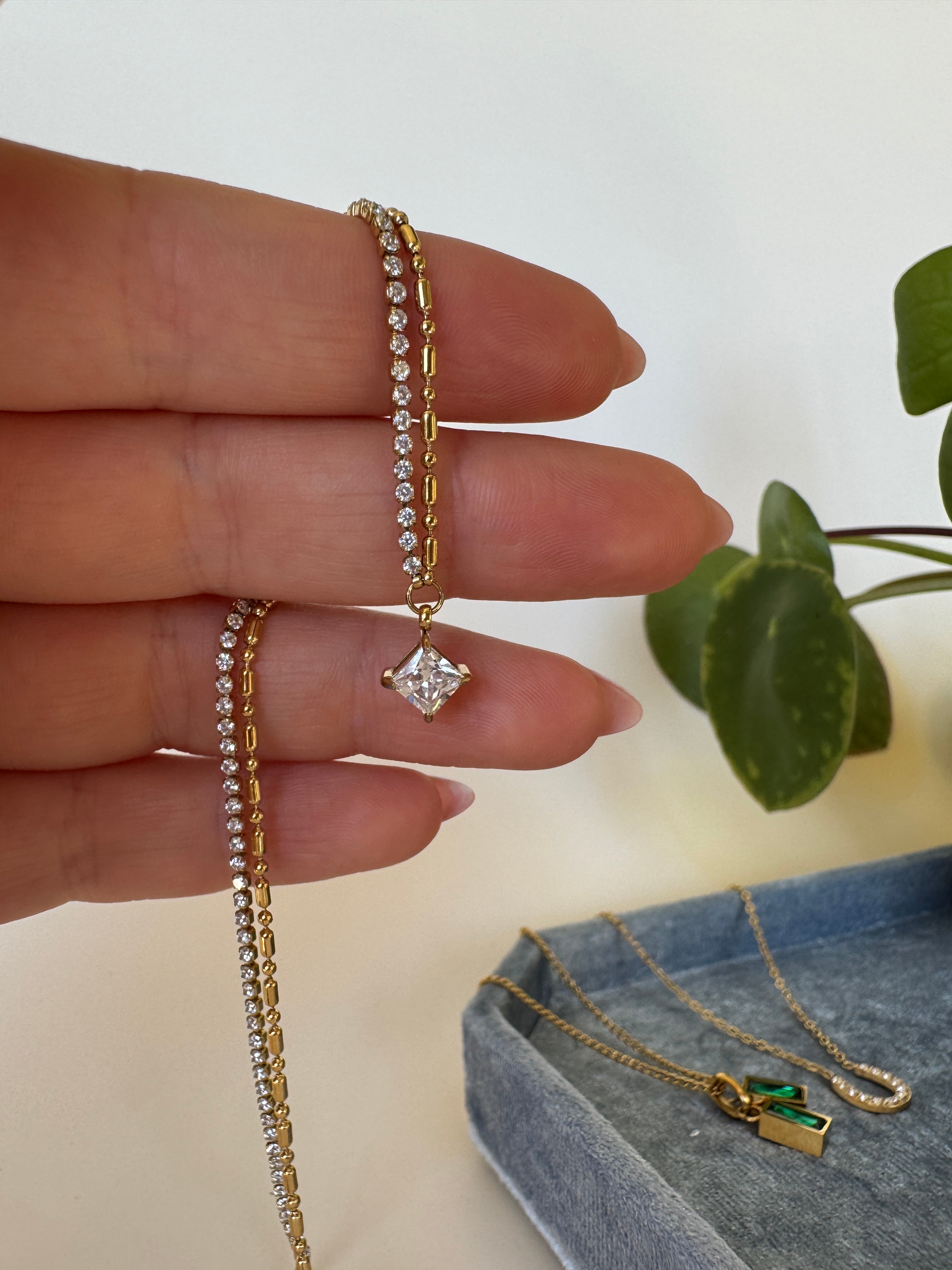 Hand wearing a diamond ring with two gold bracelets on a neutral background