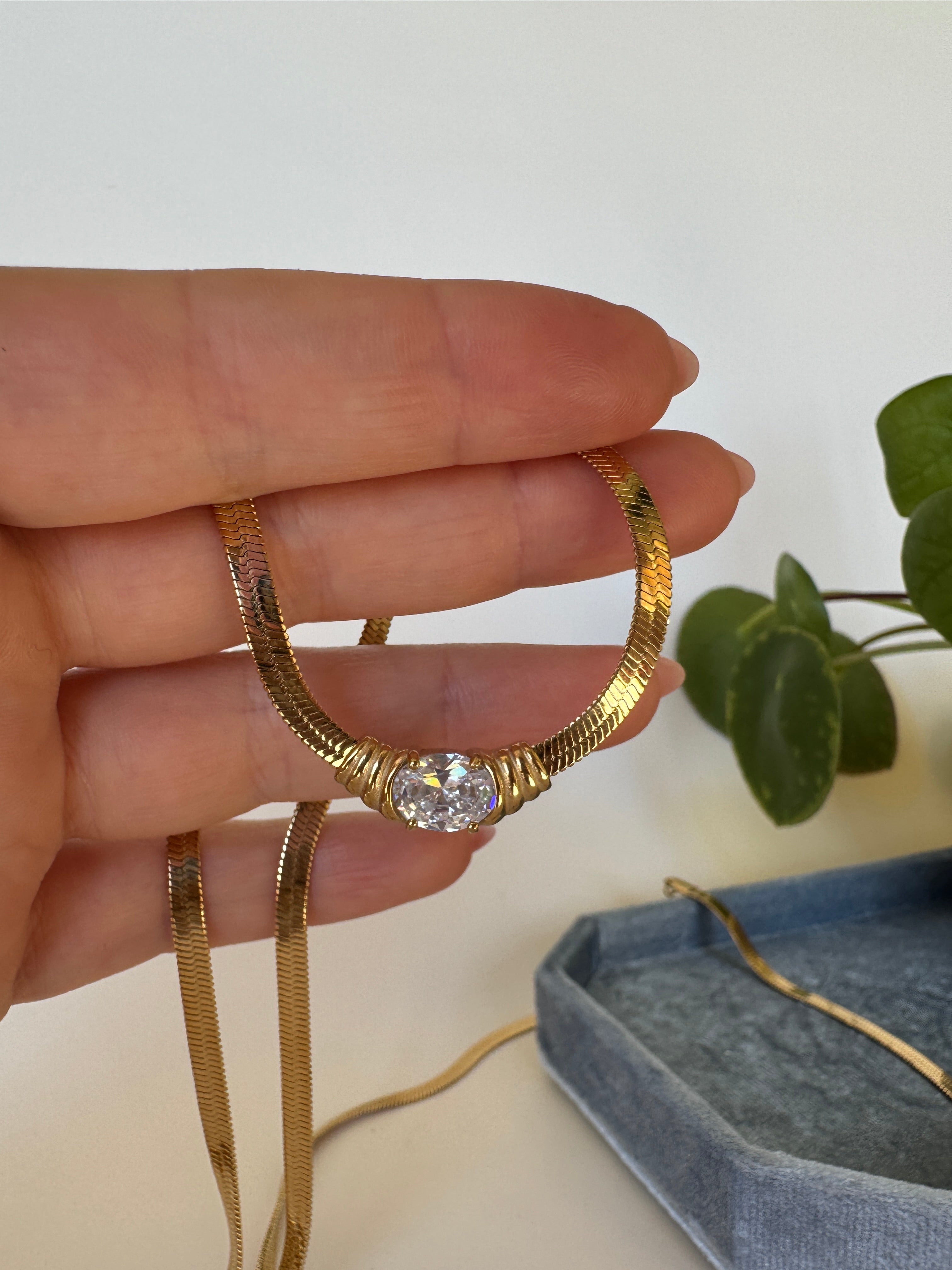 Gold necklace with white gemstone on a finger against a neutral background