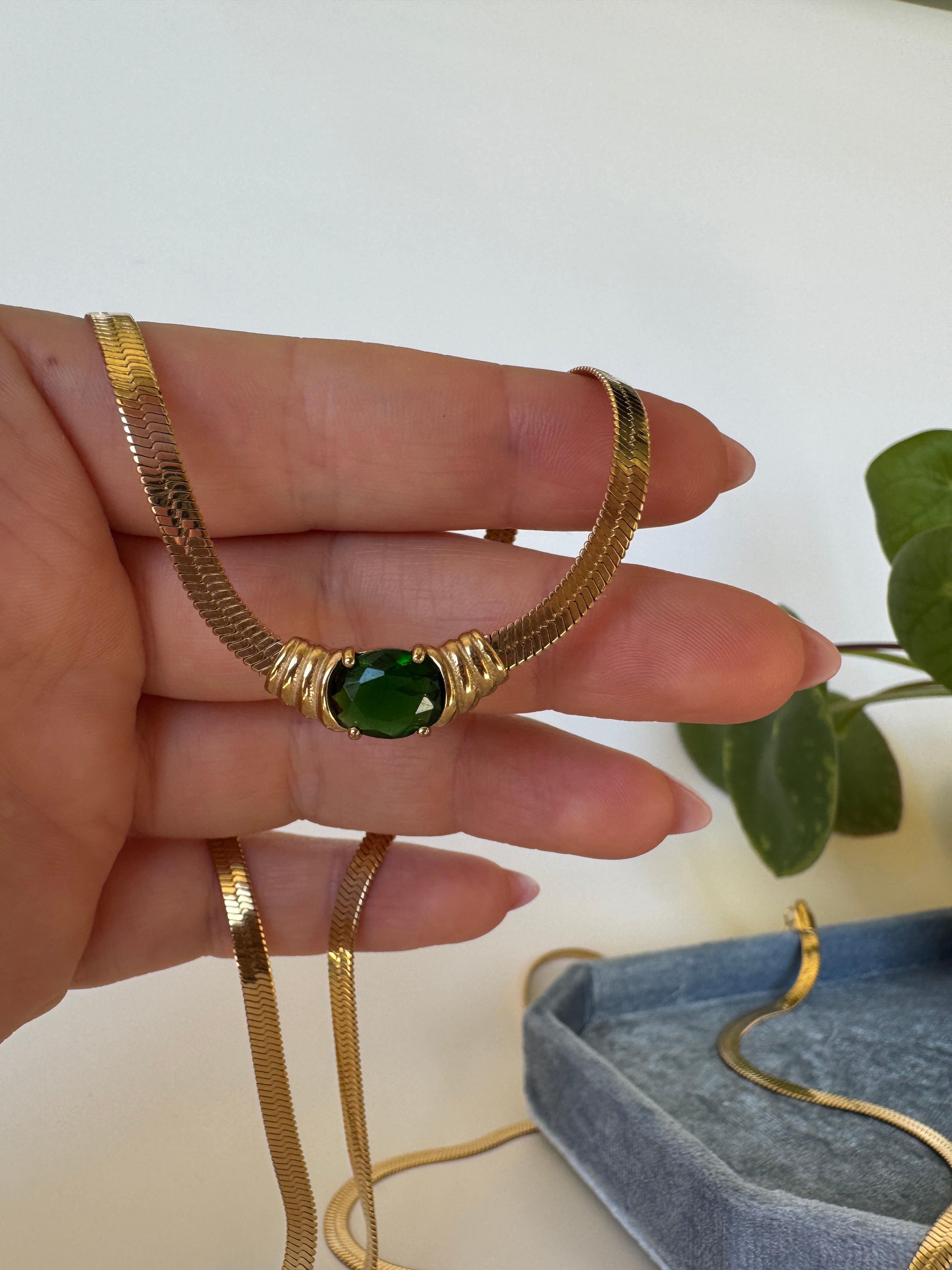 Gold necklace with a green gemstone on a hand against a neutral background