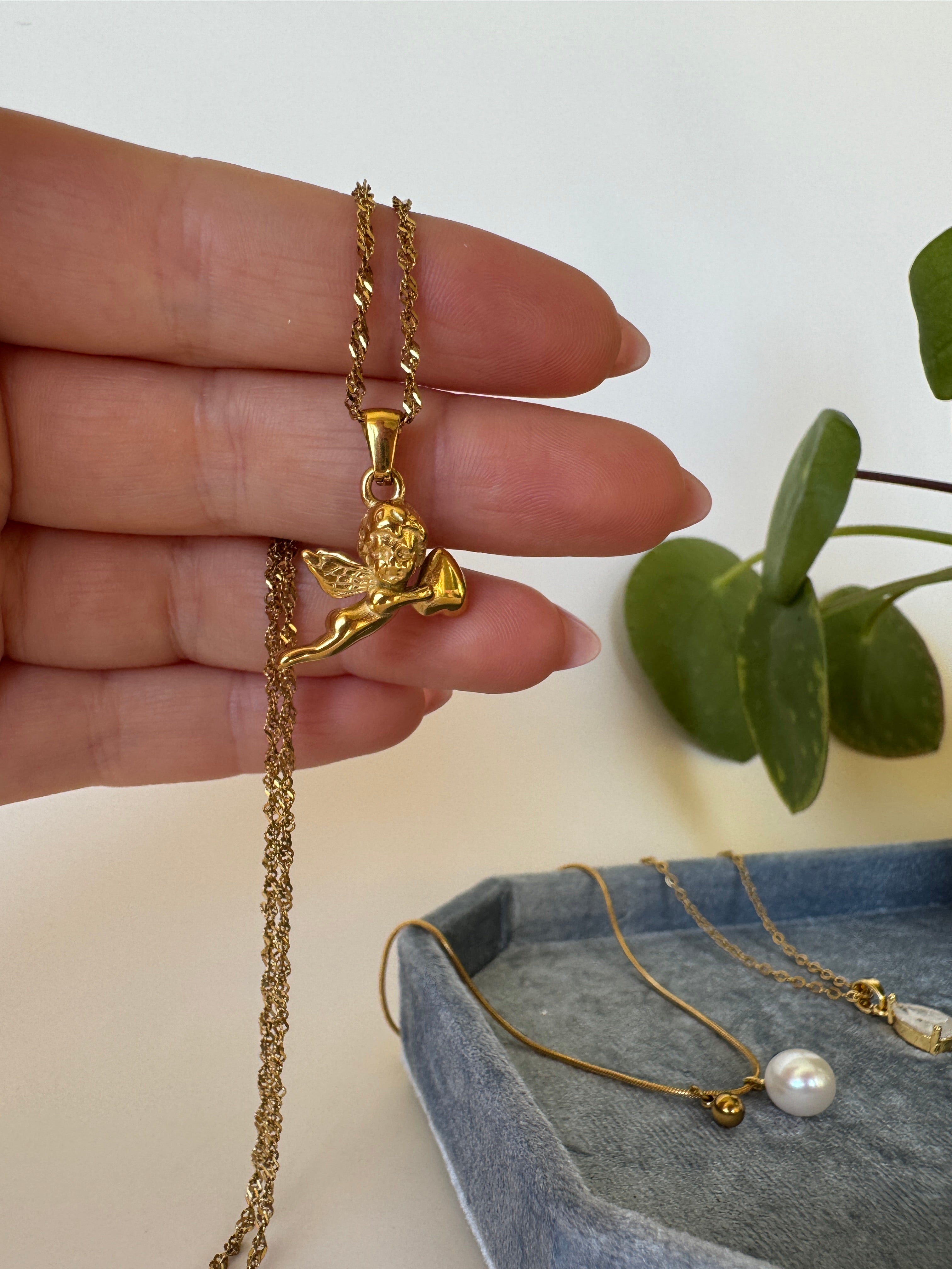 Gold necklace with angel lucky in love pendant held by a hand against a neutral background