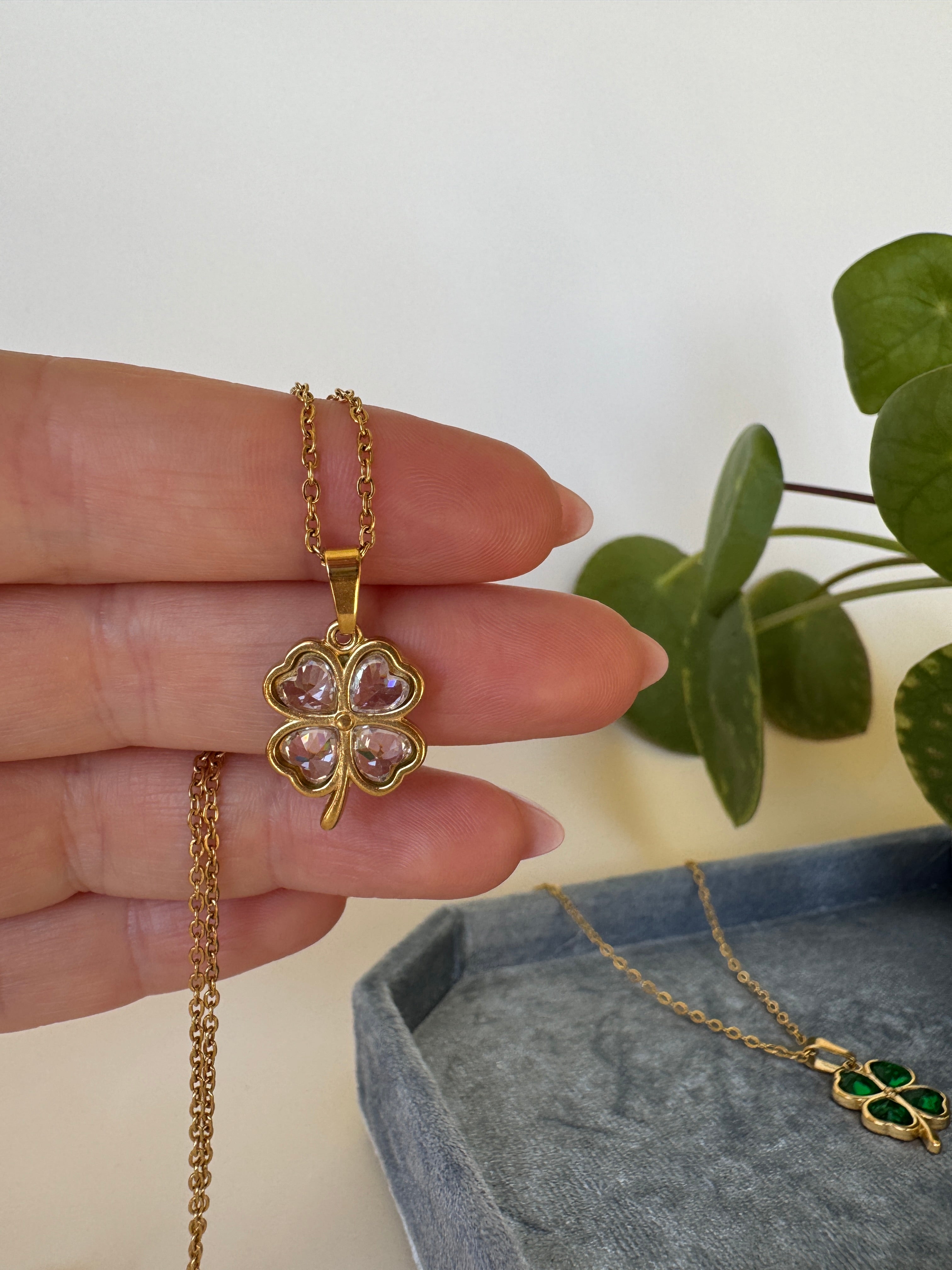 Gold lucky necklace with a clover-shaped pendant held by a hand against a neutral background.