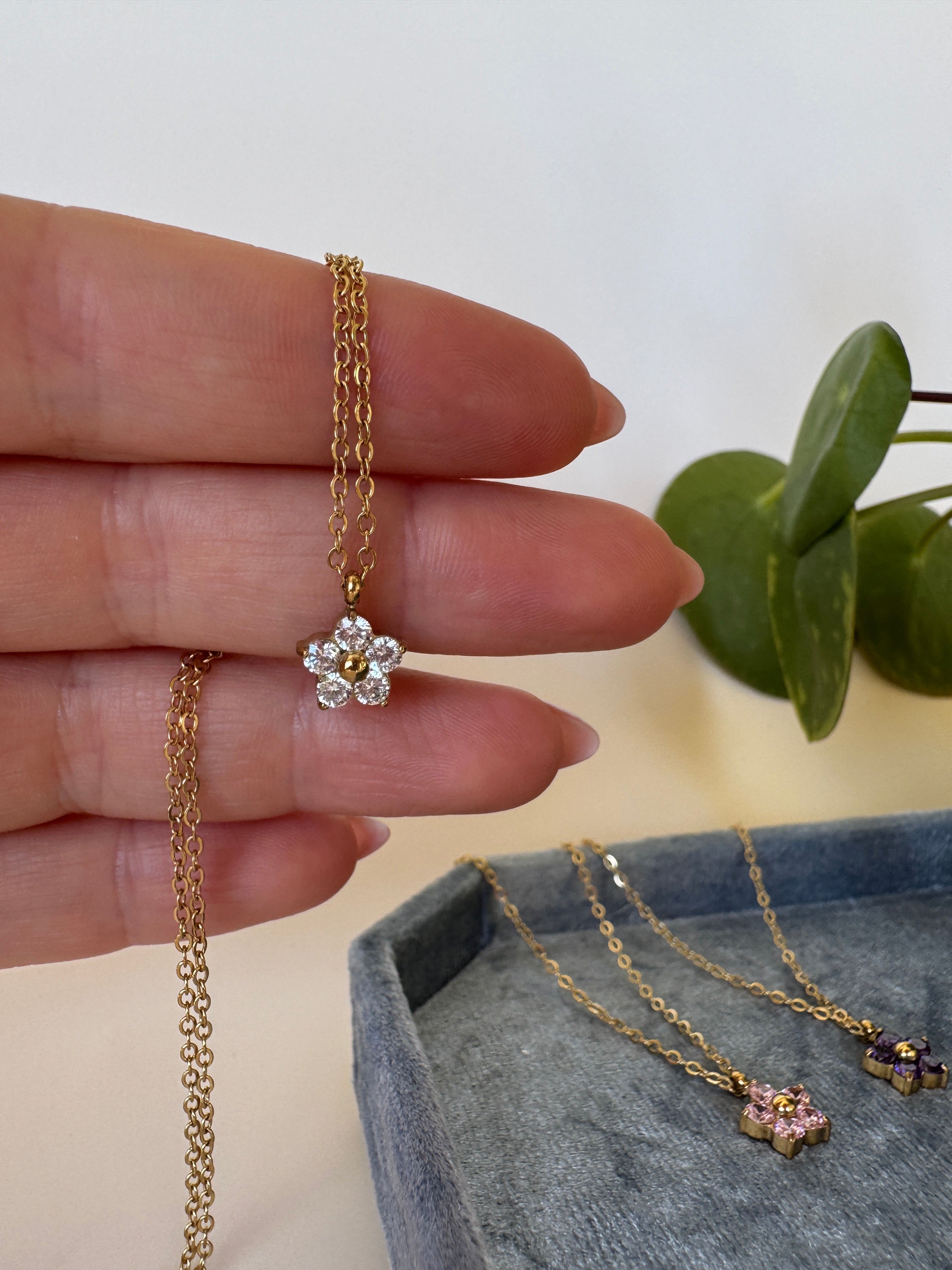 Close-up of a hand holding a gold stainless steel necklace with feminine flower design on a neutral background.