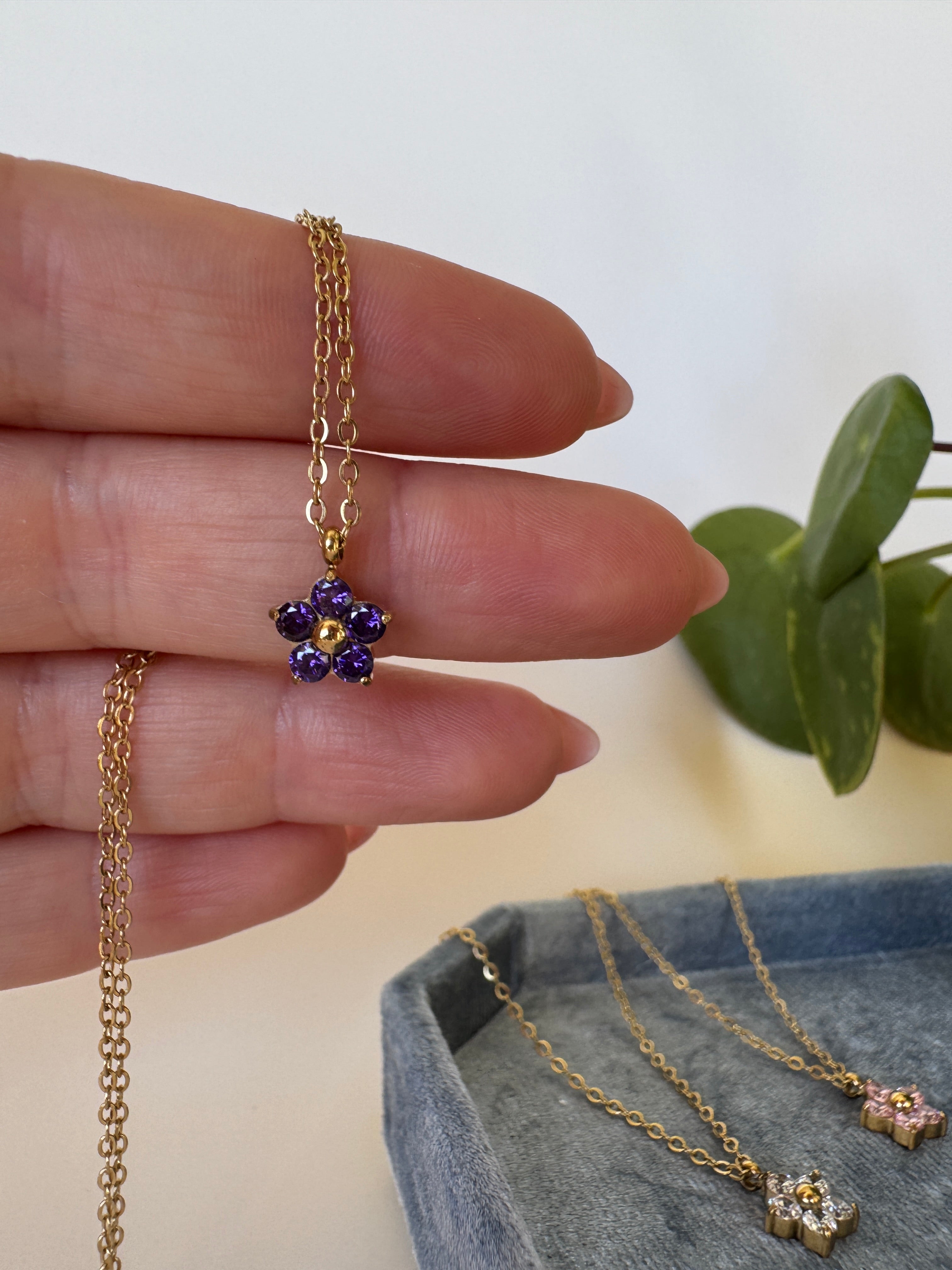 Gold waterproof necklace with a purple gemstone on a neutral background