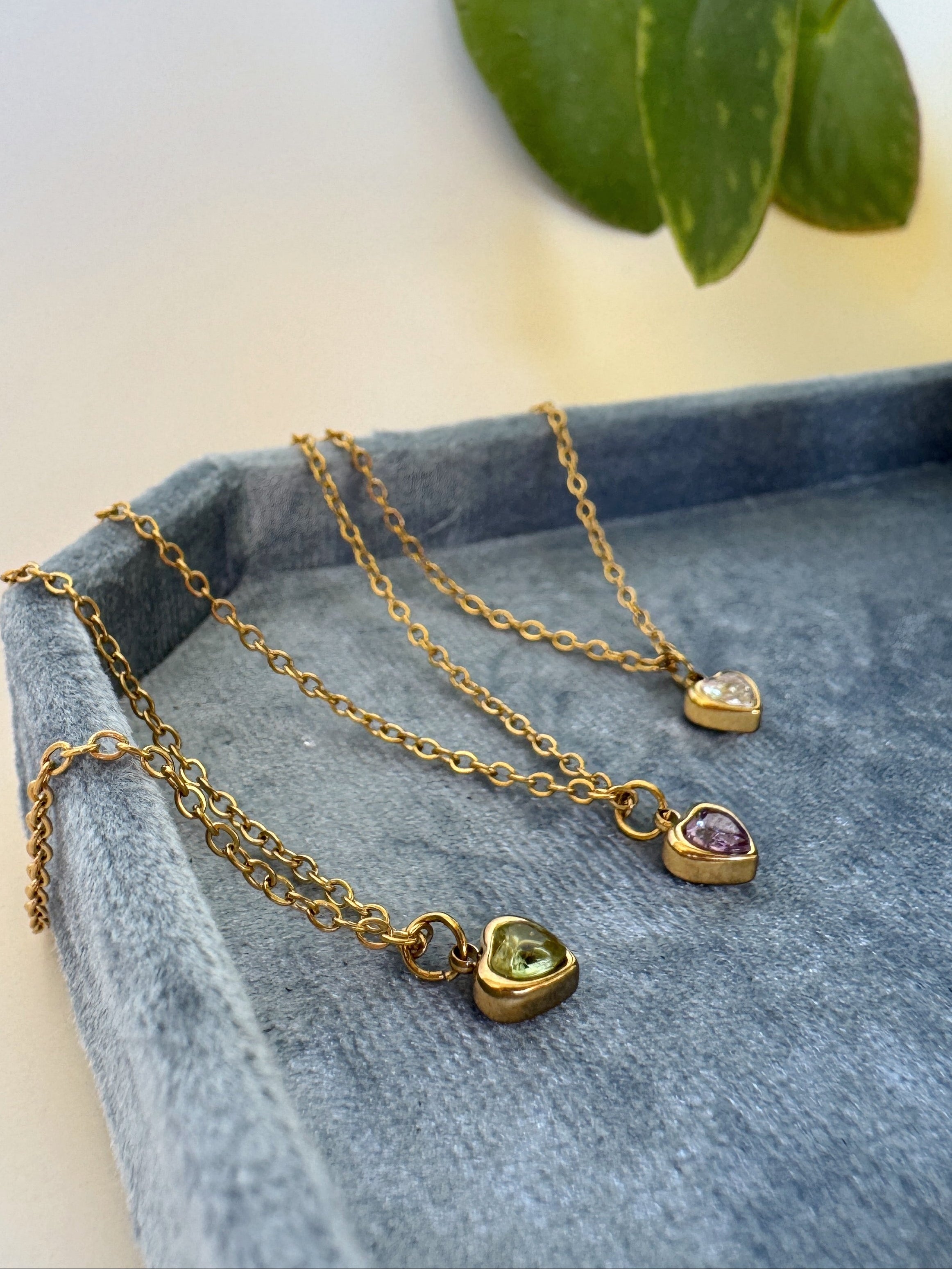 Gold necklaces with heart-shaped pendants on a blue surface with green leaves in the background