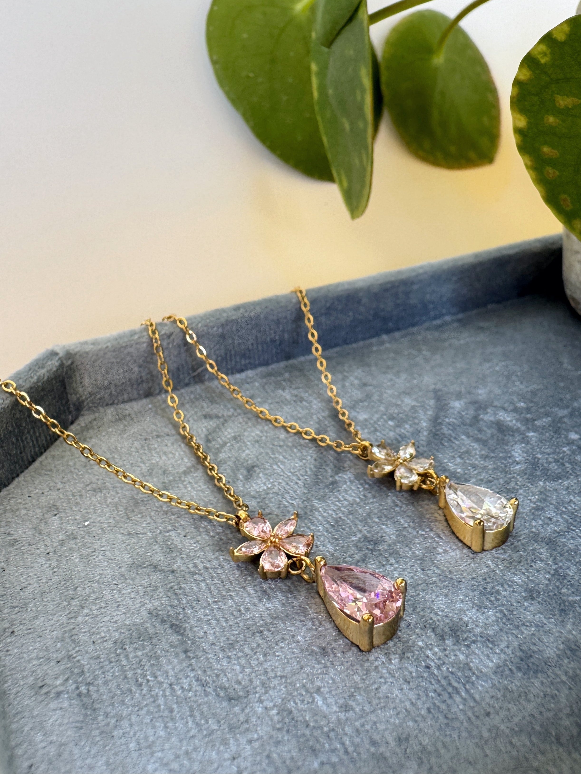 Gold necklace with pink gemstones on a gray surface with green leaves in the background