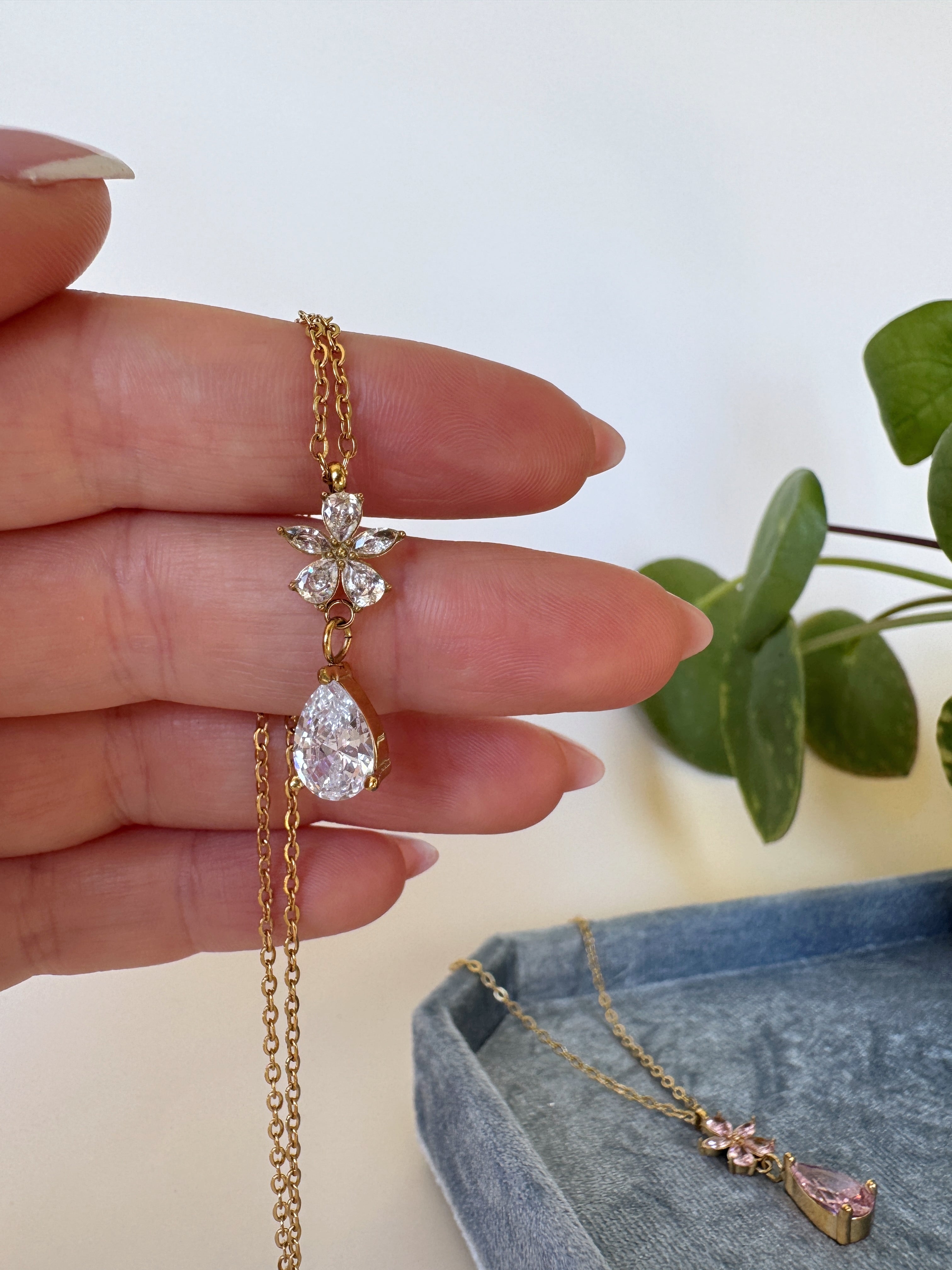 Gold necklace with a teardrop-shaped pendant held by a hand against a light background.