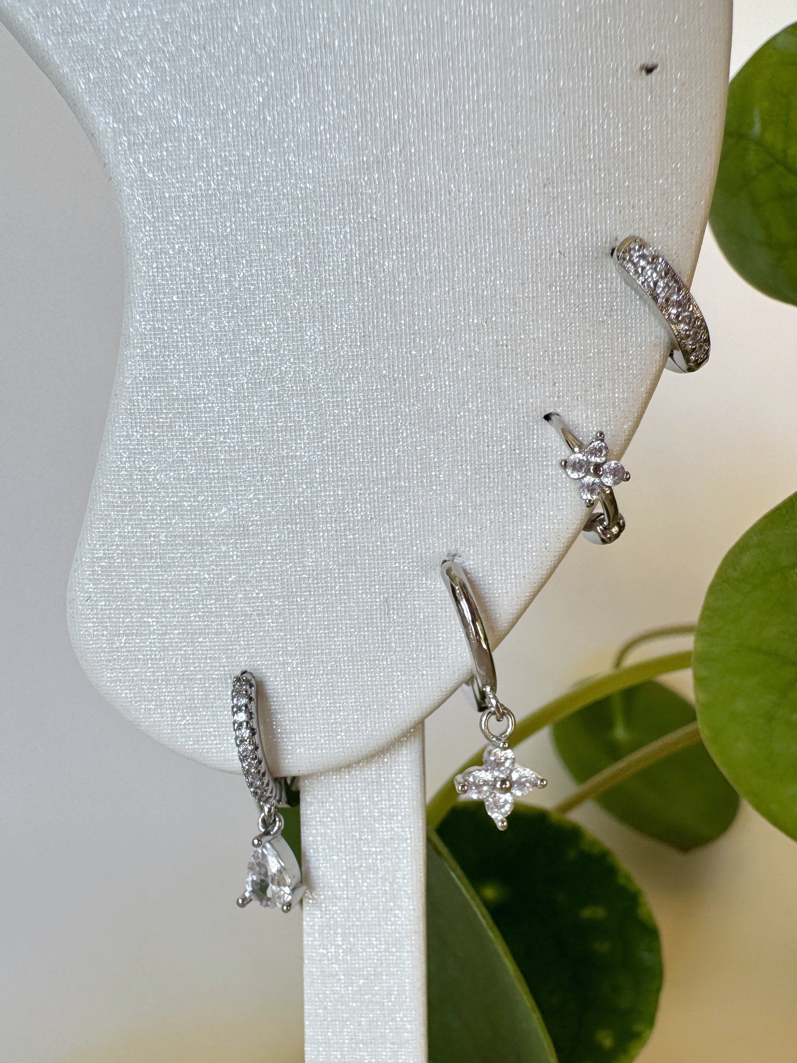 Silver earrings on a white stand with green leaves in the background