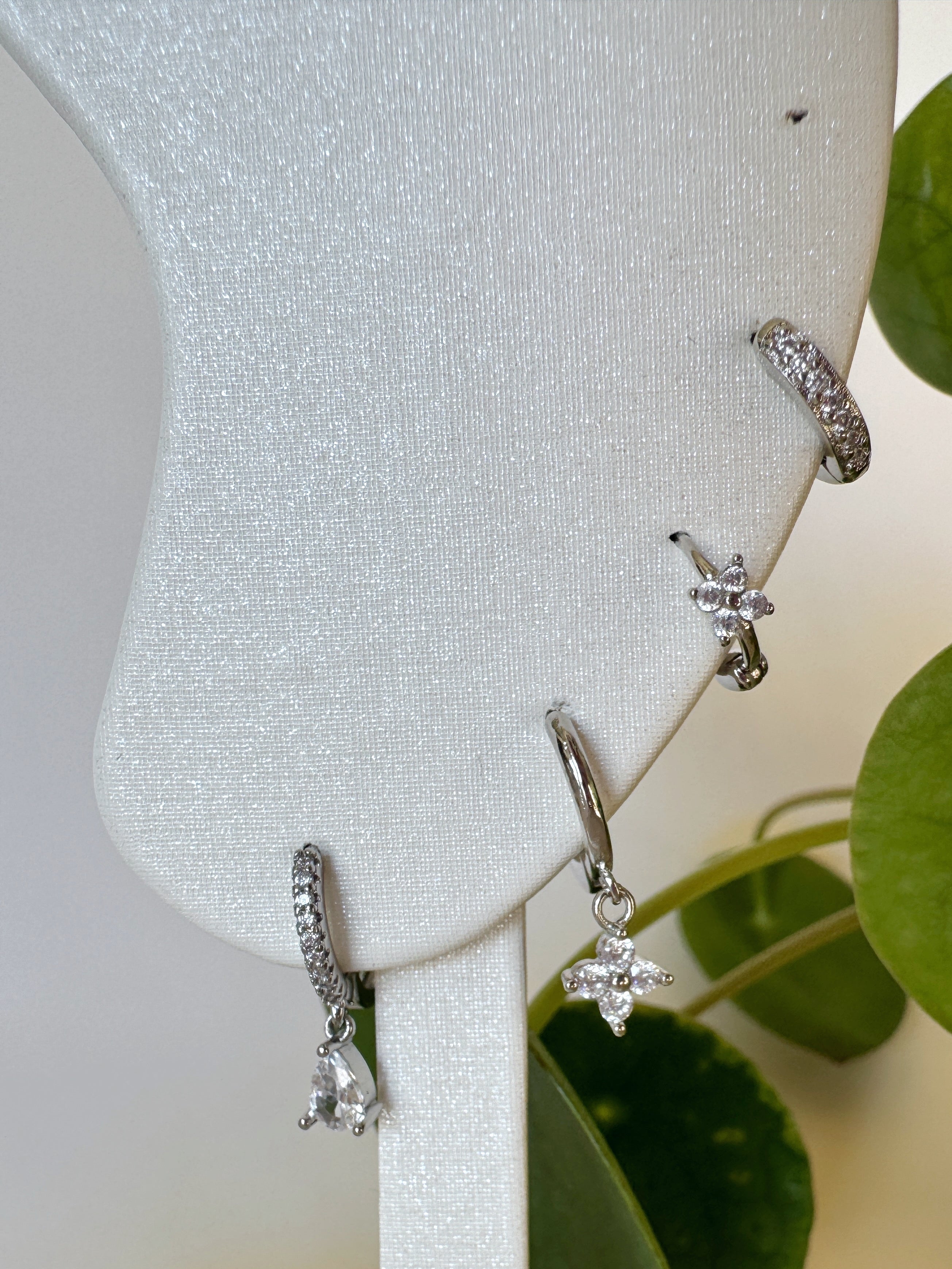Silver earrings on a white stand with green leaves in the background
