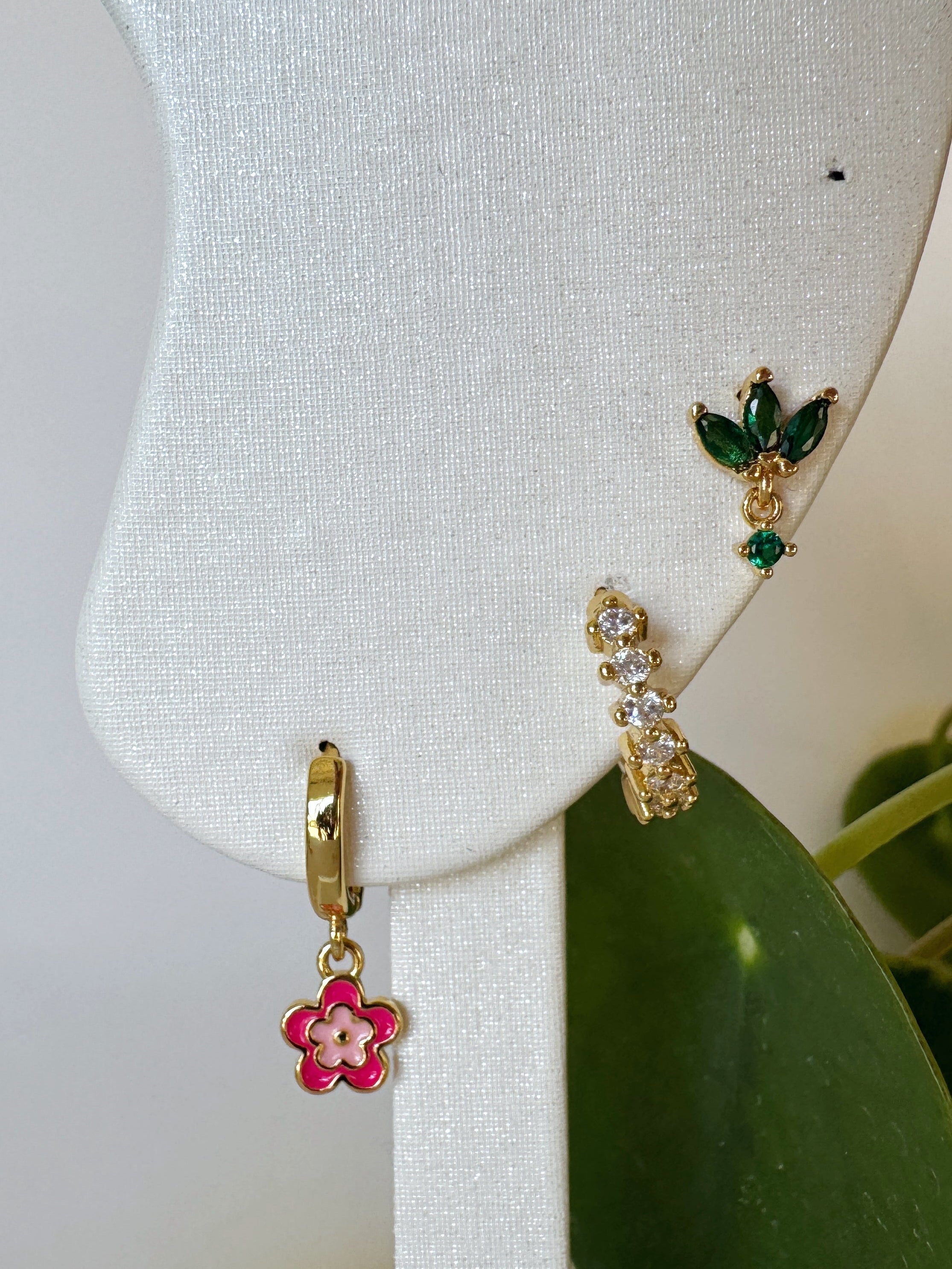 Gold, red and green floral earring on a white stand with green leaves in the background