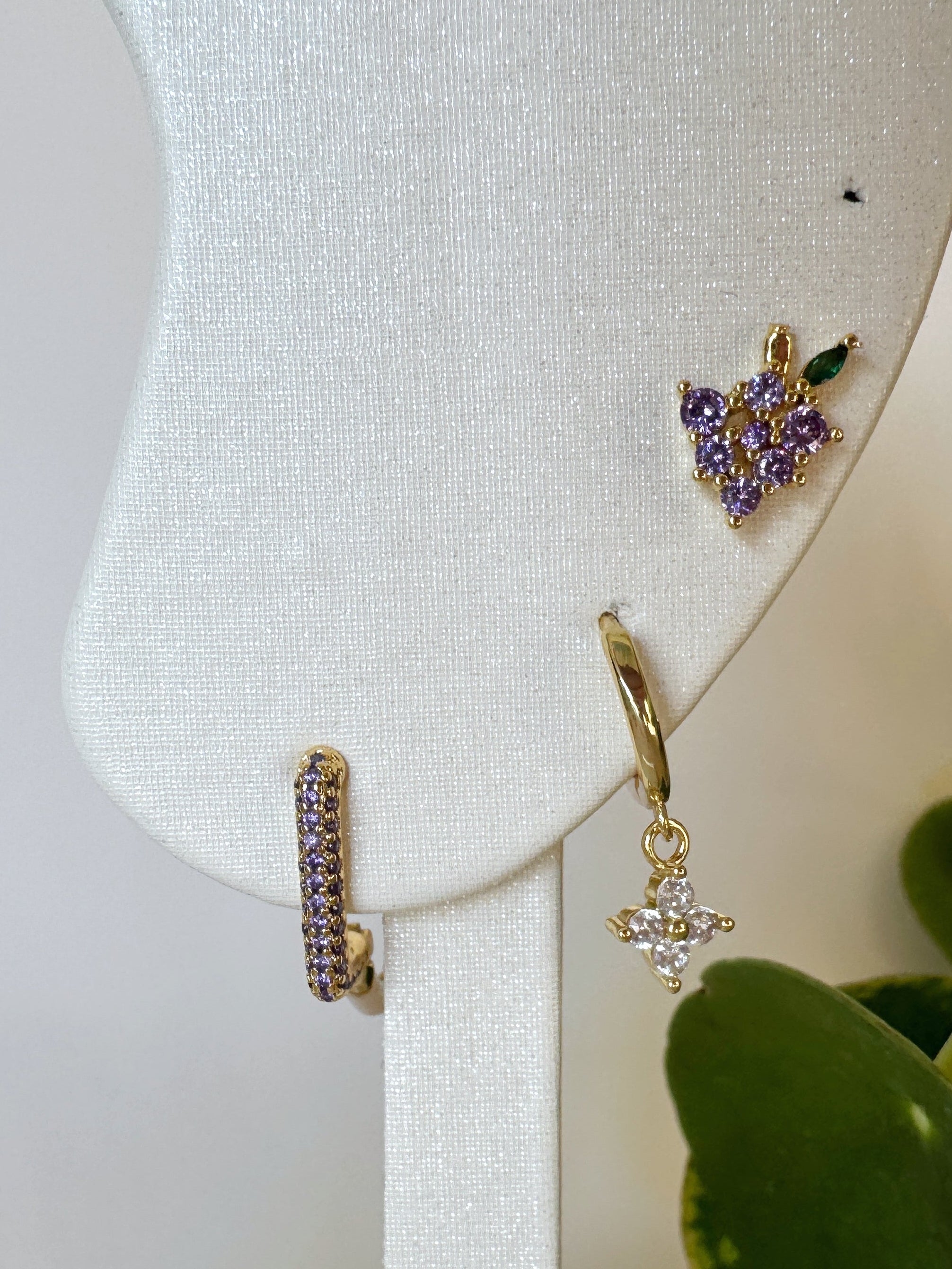 Gold earrings on a white stand with a plant in the background