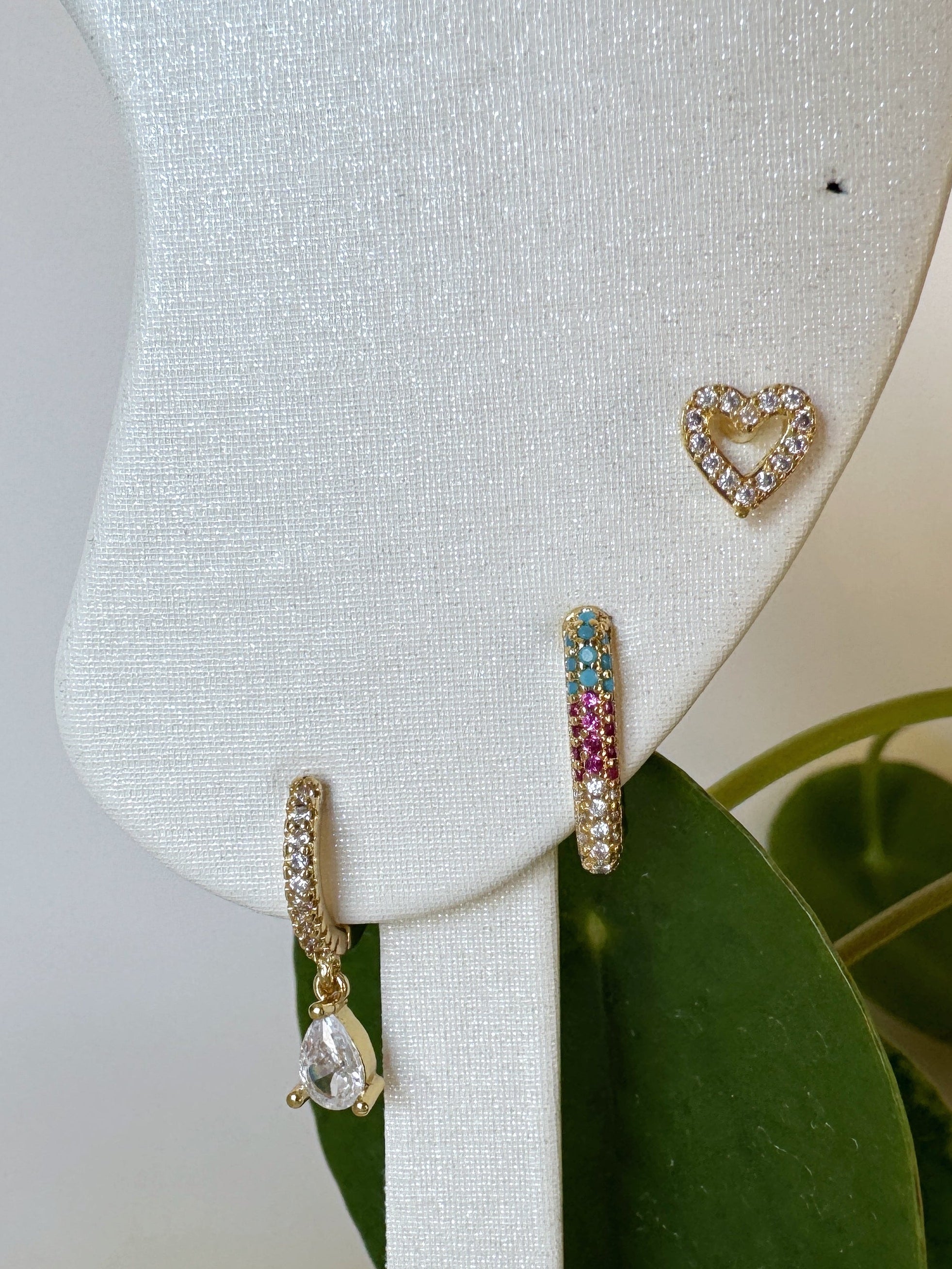 Heart-shaped earrings on a white mannequin bust with green leaves in the background
