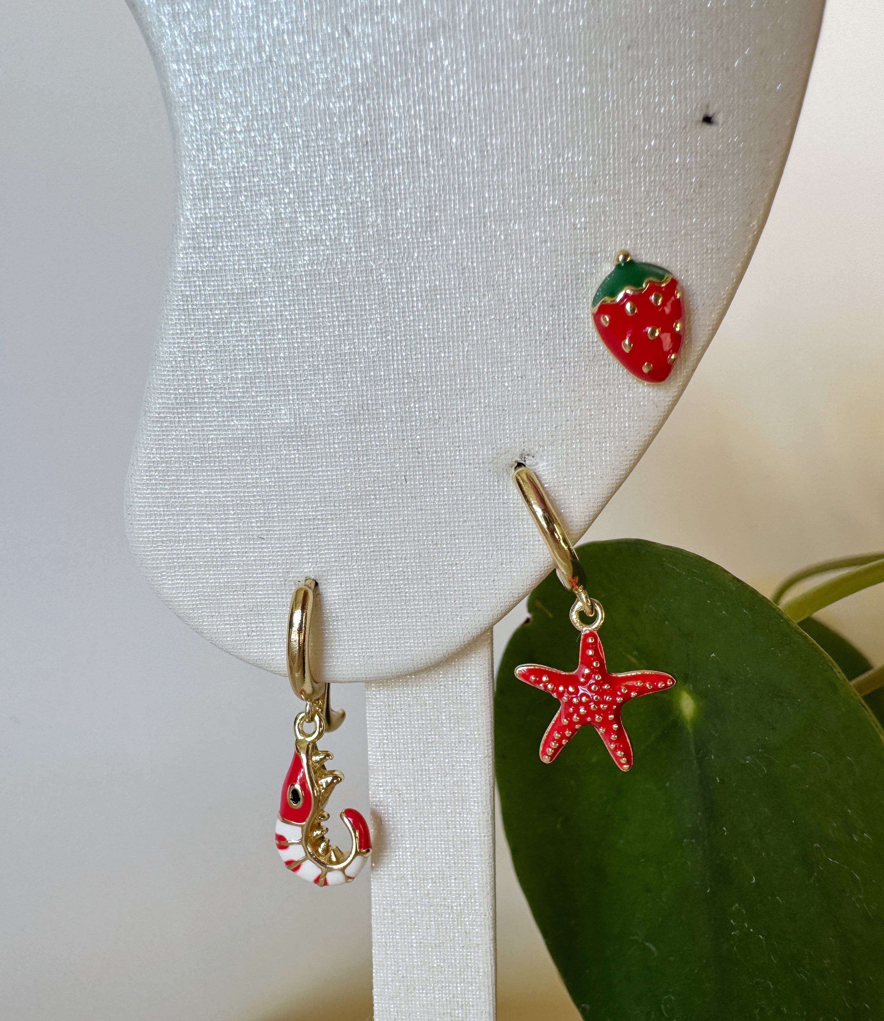 Two earrings on a white stand with a green leaf background