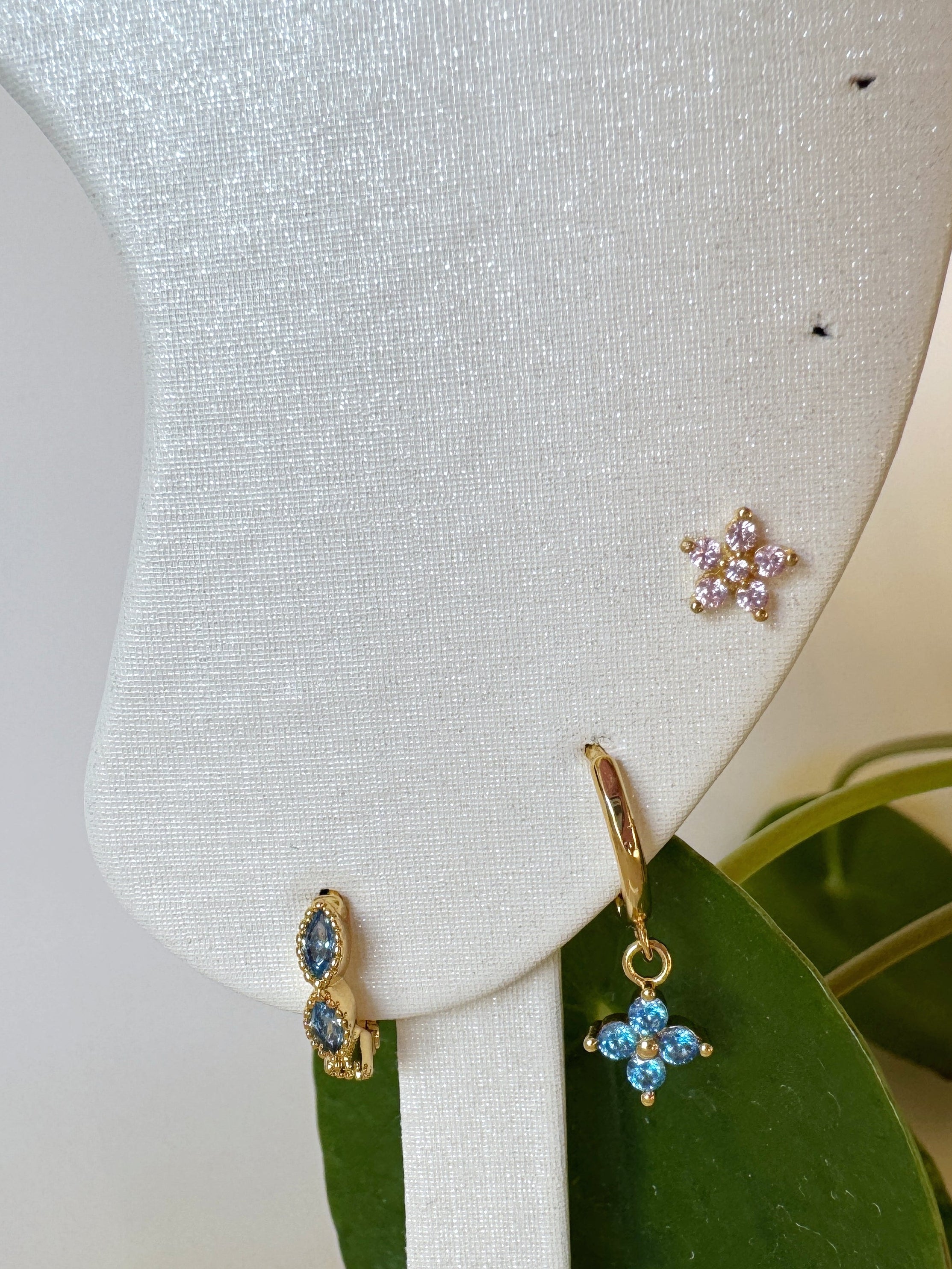 Gold earrings with blue stones on a white jewelry display stand.