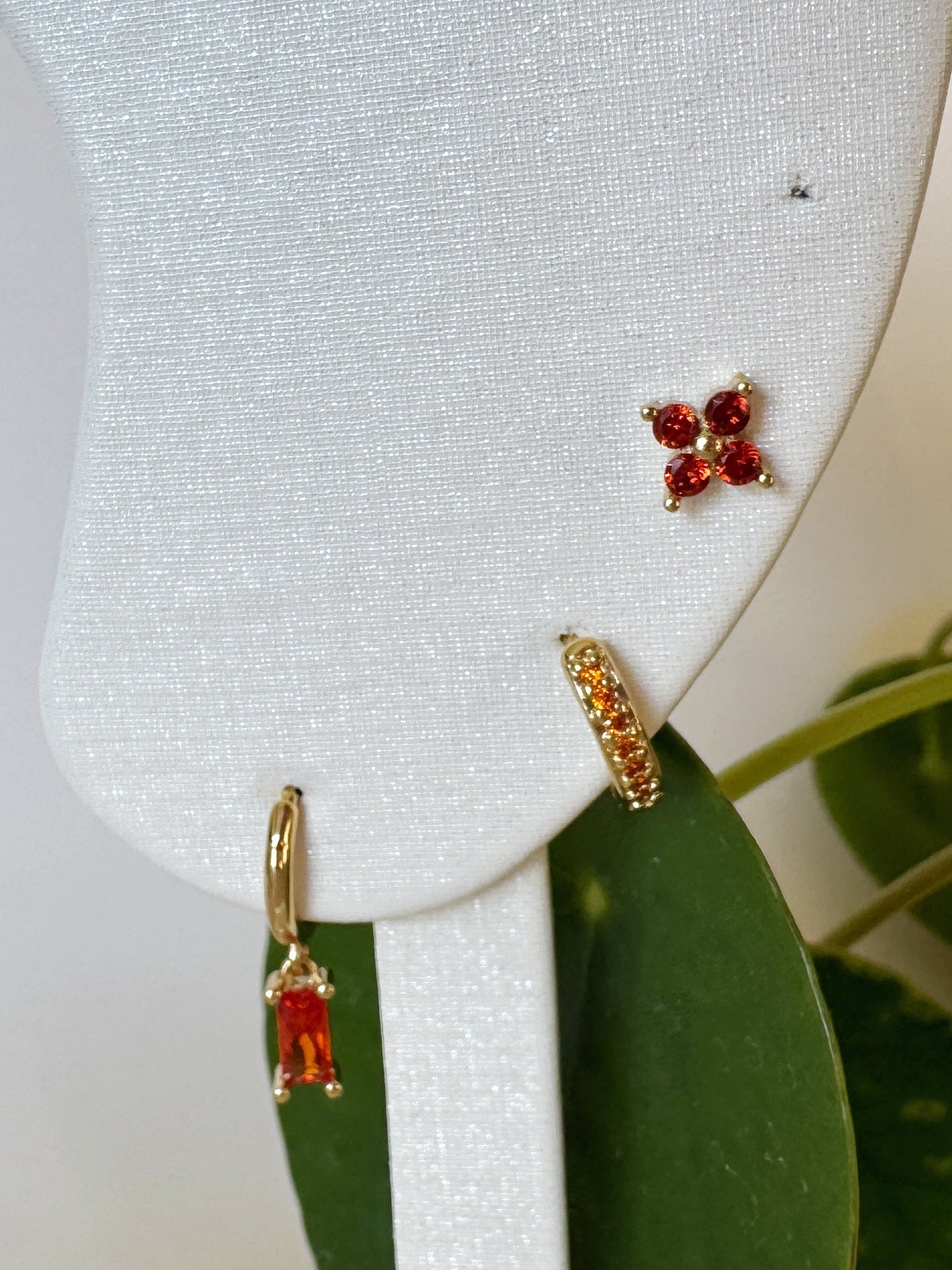 Orange gemstone earrings on a white earring stand with green leaves in the background