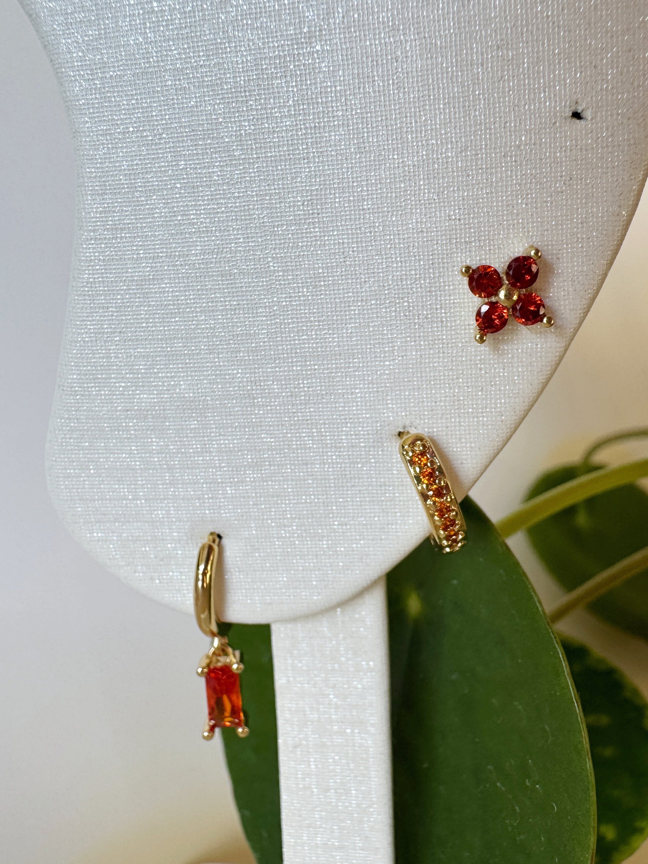 Pair of orange gemstone earrings on a white earring stand with green leaves in the background.