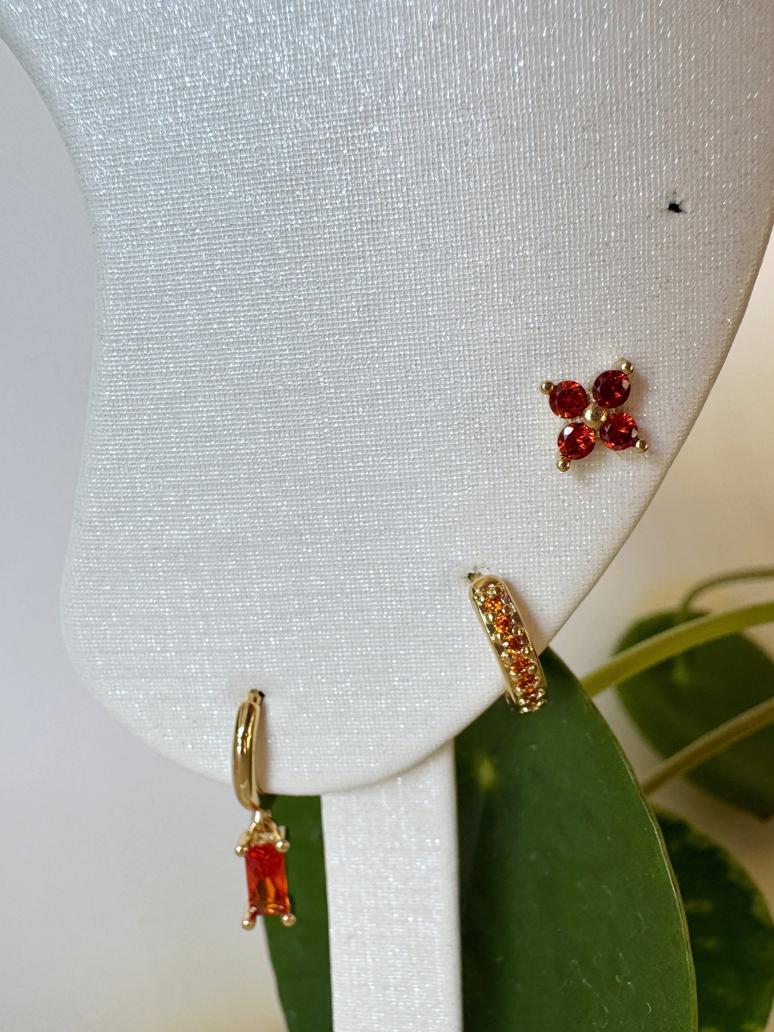 Pair of orange gemstone earrings on a white earring stand with green leaves in the background