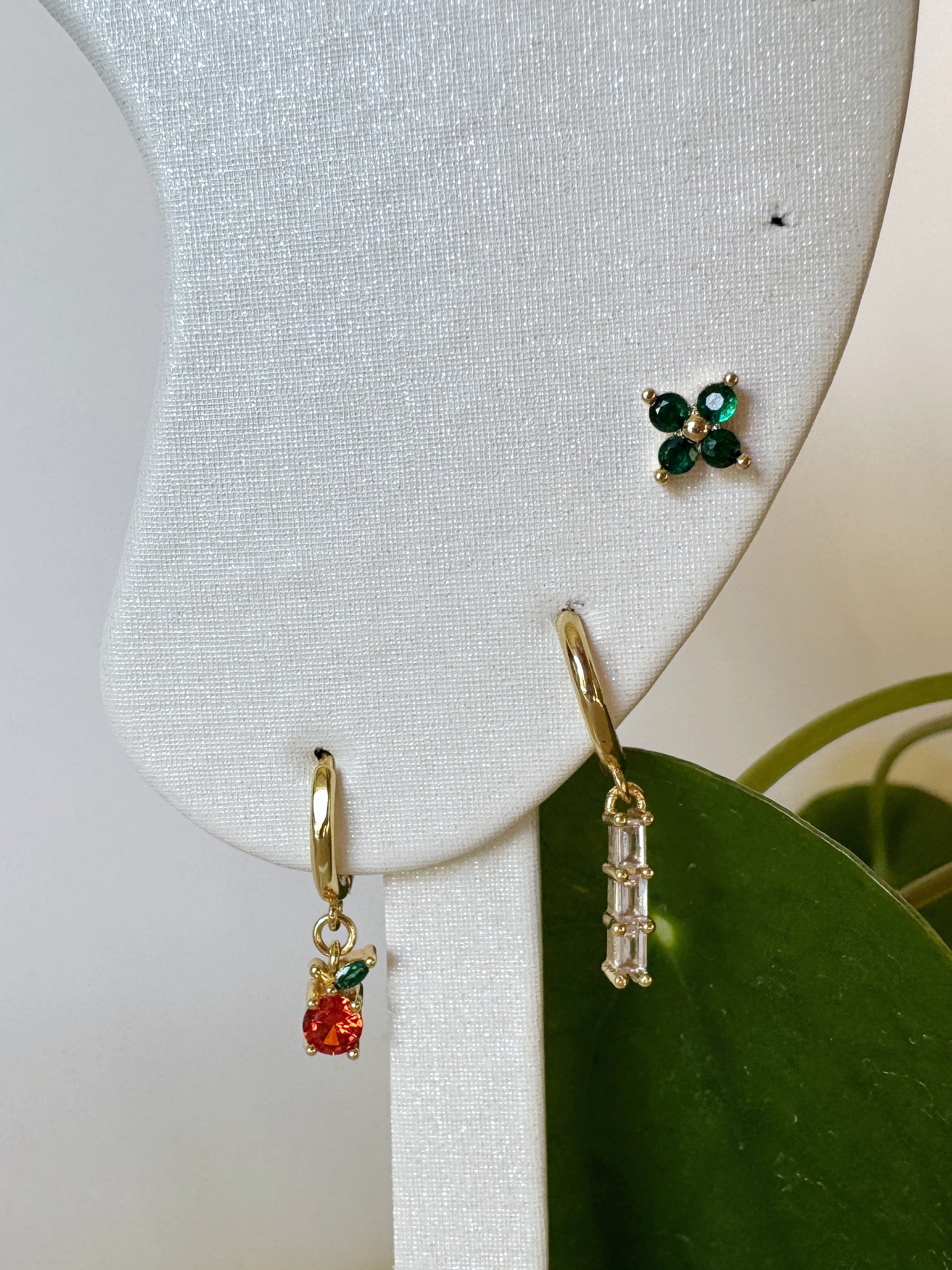 Three pairs of earrings on a white jewelry display with green leaves in the background