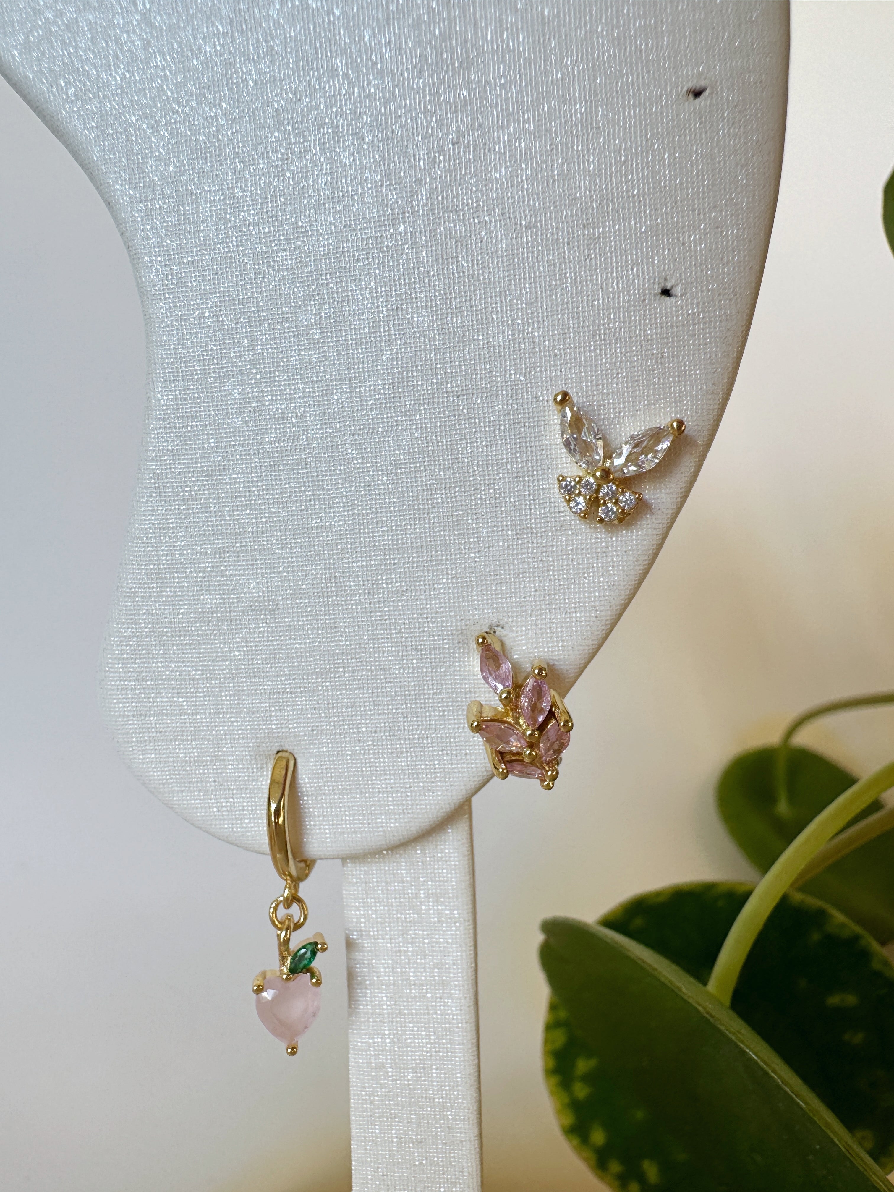 Gold earrings with pink stones on a white stand with a plant in the background