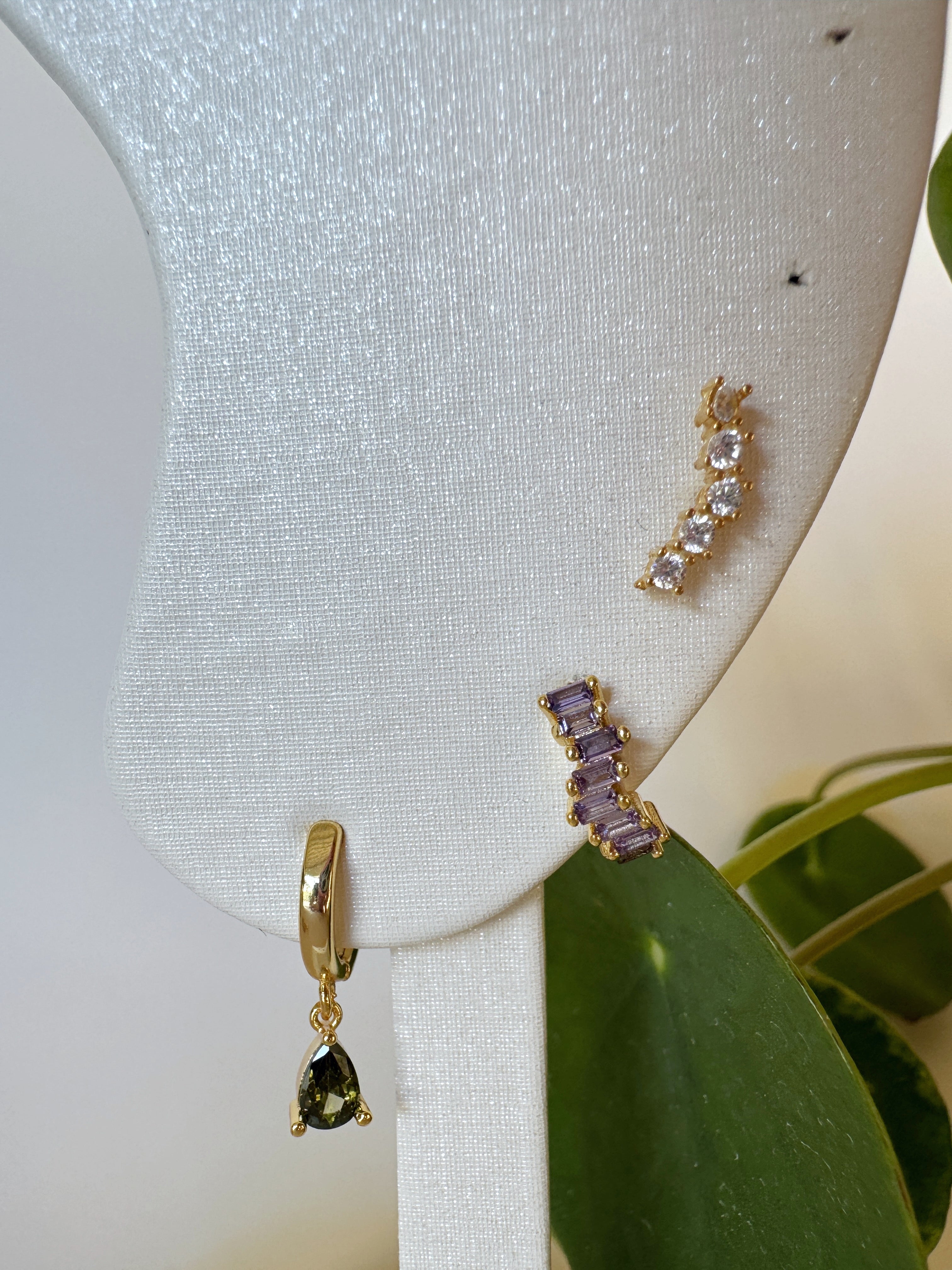 Gold and purple earrings on a white stand with a green leafy background
