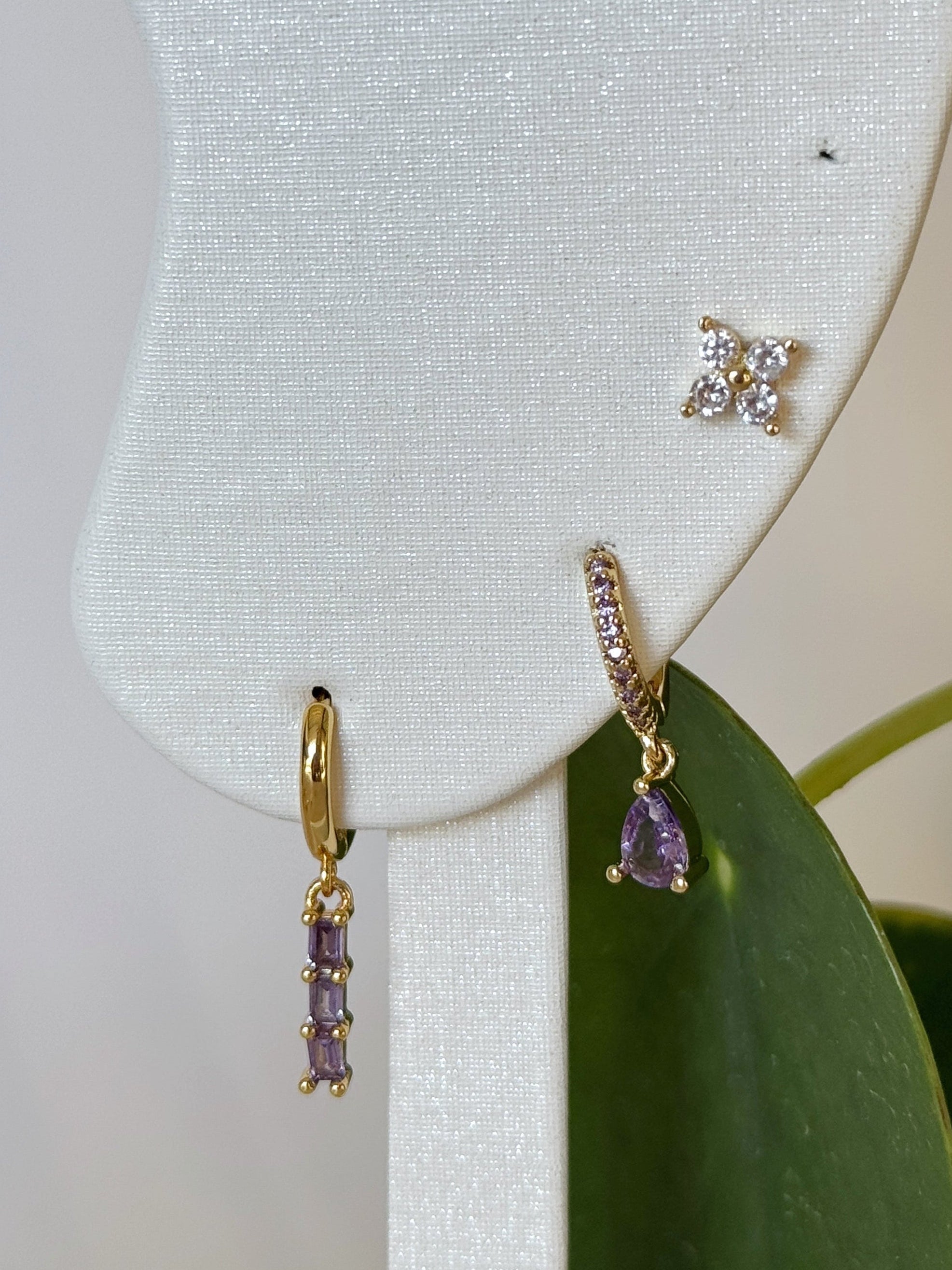 Gold earrings with gemstones on a white earring stand with a green leaf background